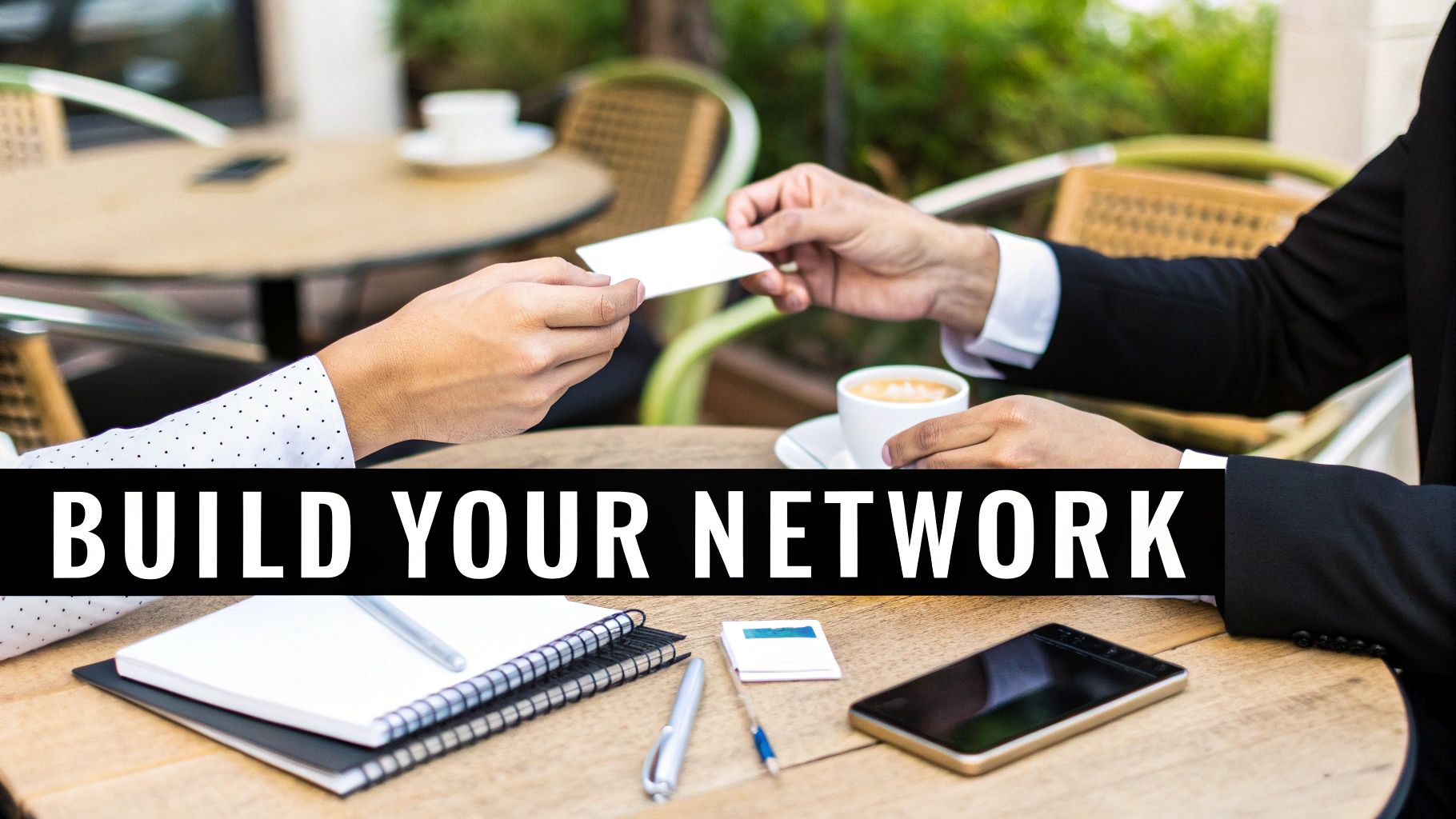 Hands exchanging a business card over a cafe table with coffee, notebooks, and a smartphone, symbolizing networking.
