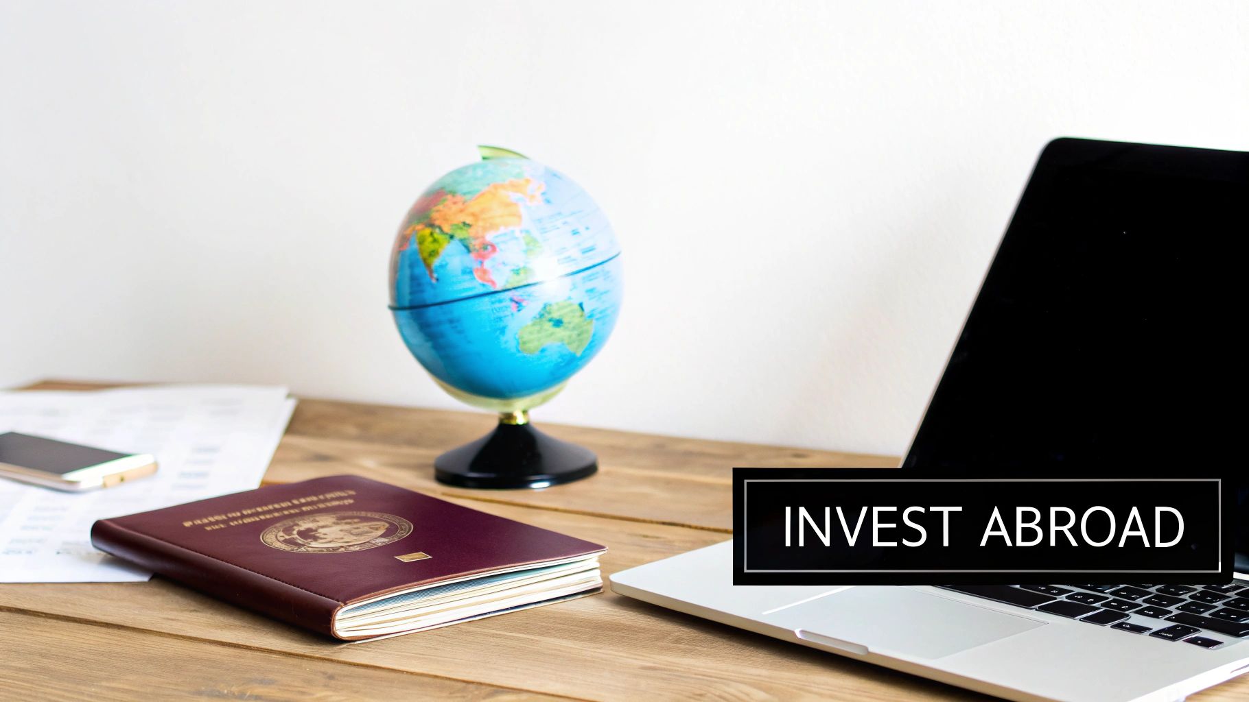 A desk with a passport, globe, and laptop, featuring an 'INVEST ABROAD' text overlay.