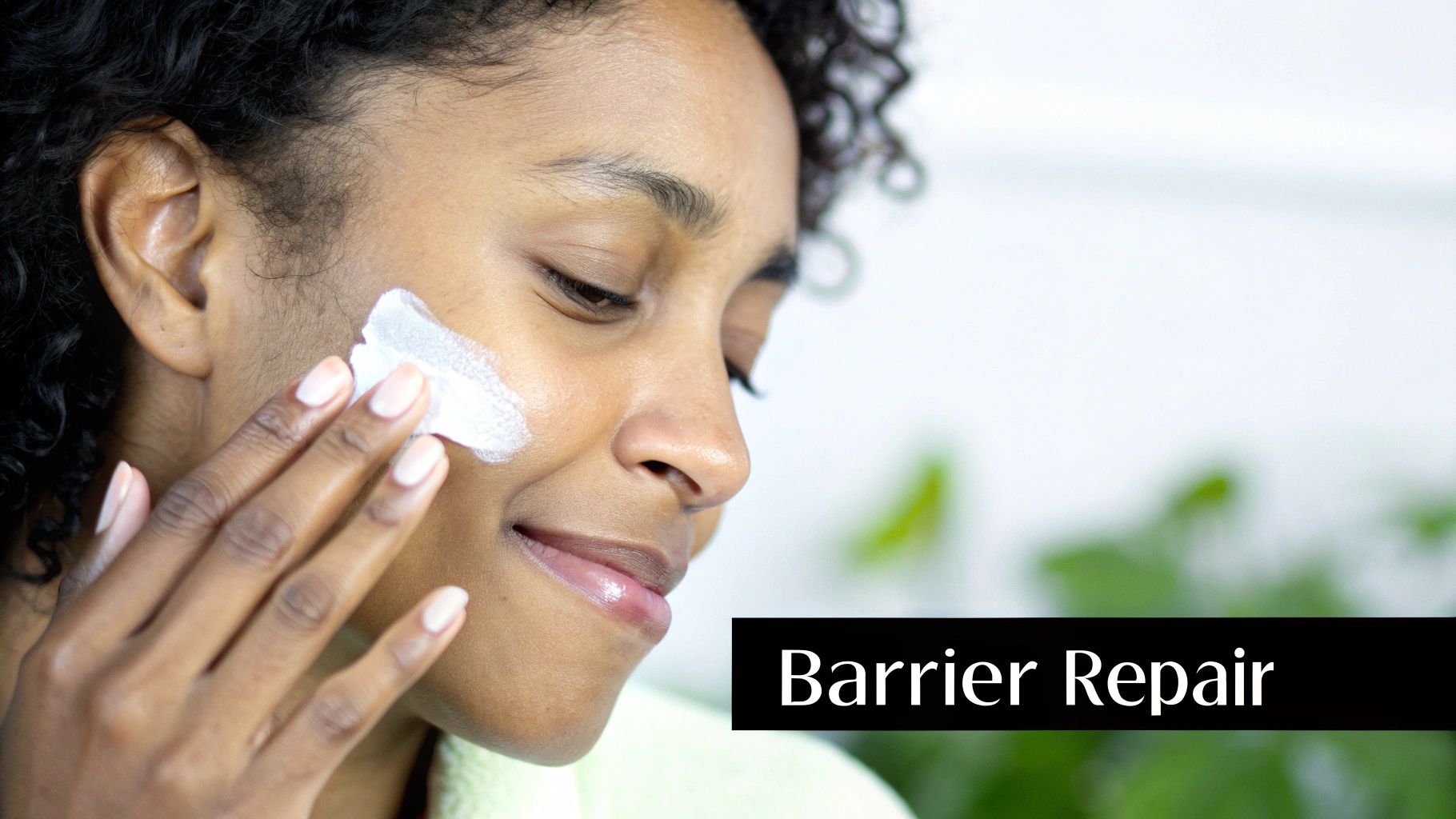 A smiling woman with curly hair applies white barrier repair cream to her cheek.