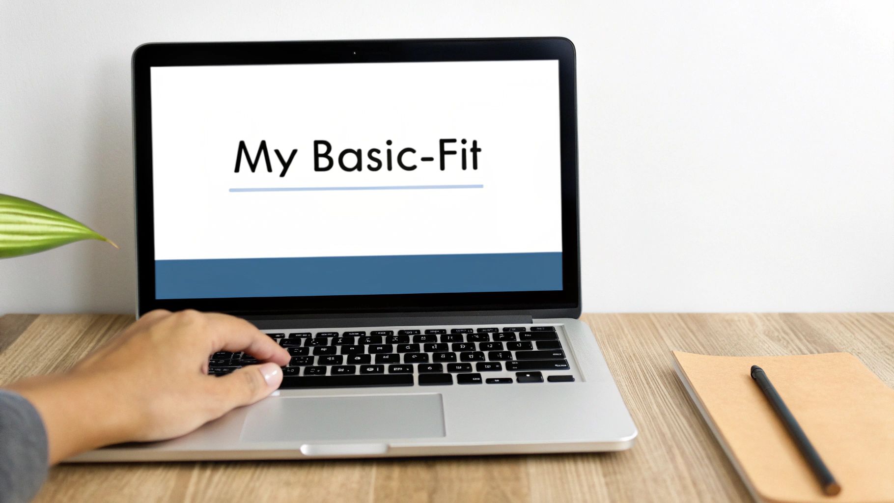 Een persoon typt op een laptop met 'My Basic-Fit' op het scherm, naast een plant en notitieboekje.