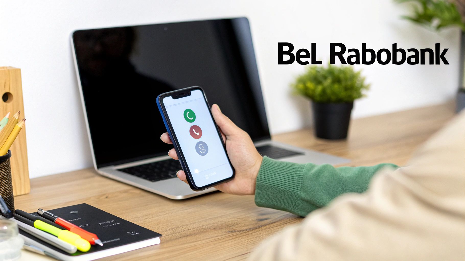 Een persoon houdt een telefoon vast met oproepknoppen. Op de achtergrond een laptop en de tekst 'Bel Rabobank'.
