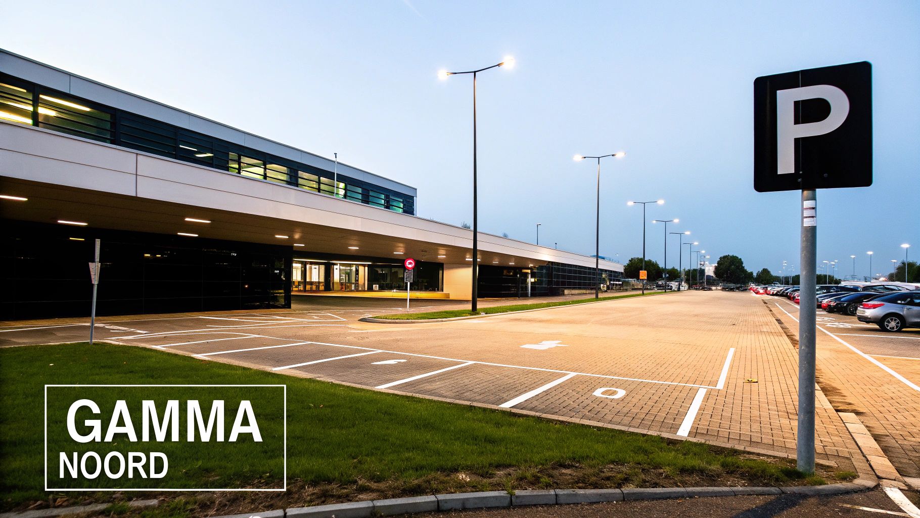 Ruime parkeerplaats met moderne gebouw en brandende straatverlichting bij schemering.