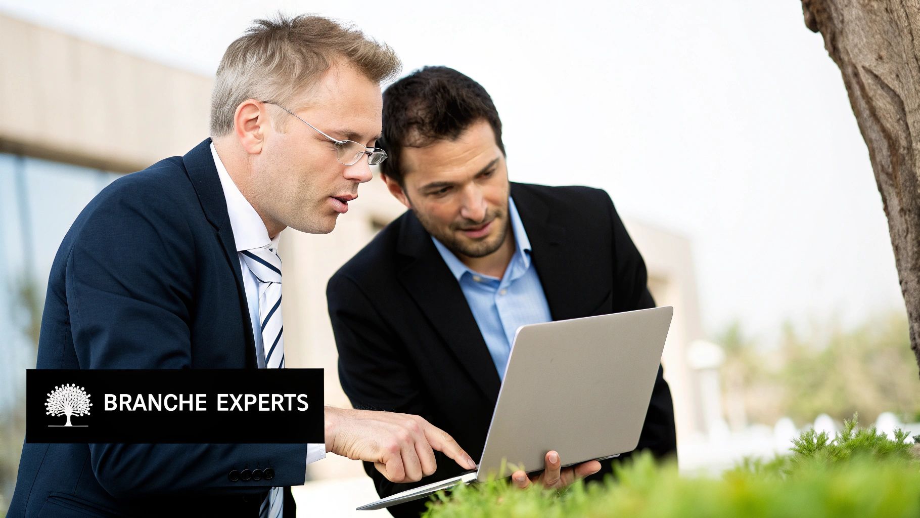 Twee zakenmannen in pak kijken naar een laptop buiten, één wijst naar het scherm.