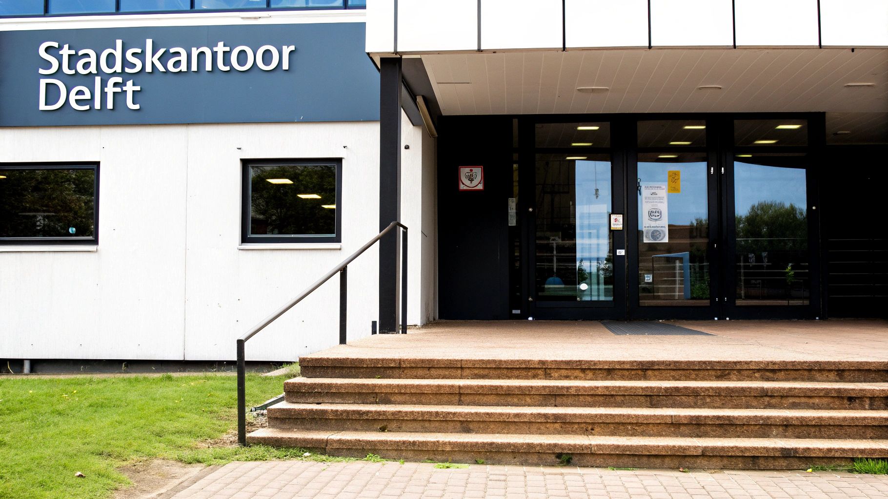 Ingang van het Stadskantoor Delft met trap, balustrade en glazen deuren.