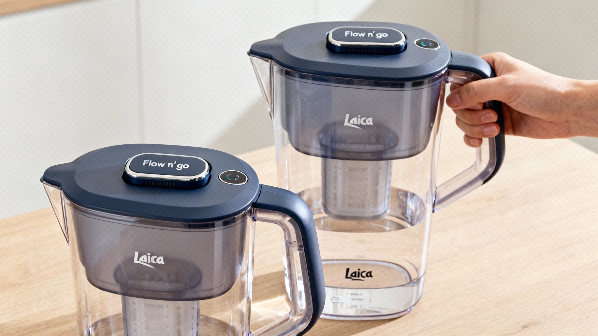 Two Laica Flow n' go water filter pitchers on a wooden counter, one held by a hand.