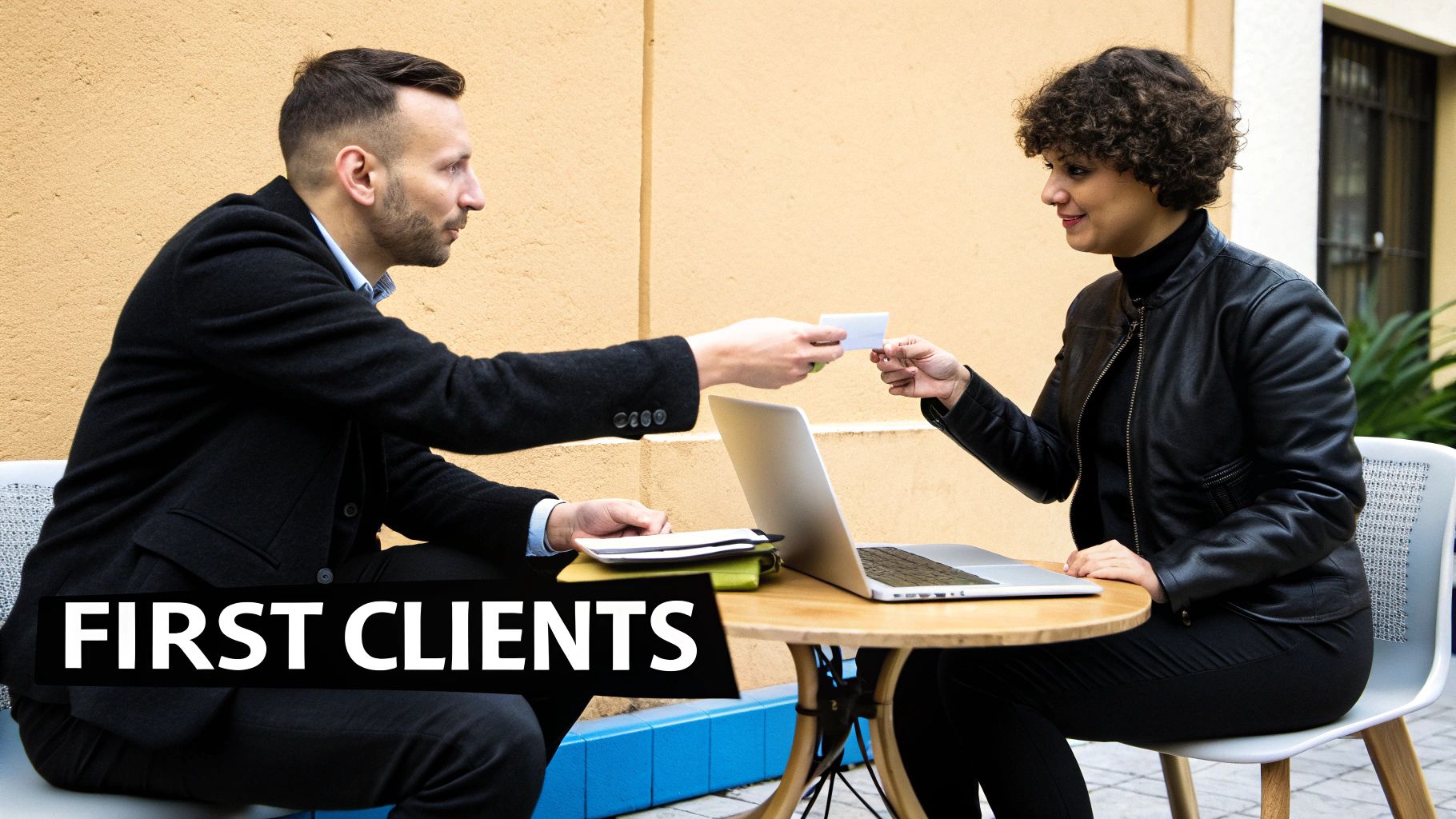 A man hands a business card to a woman during an outdoor client meeting with a laptop.