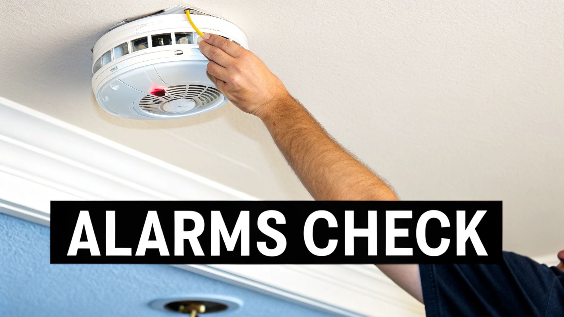 A person's arm is seen checking a white smoke detector on a ceiling, with a red indicator light visible.