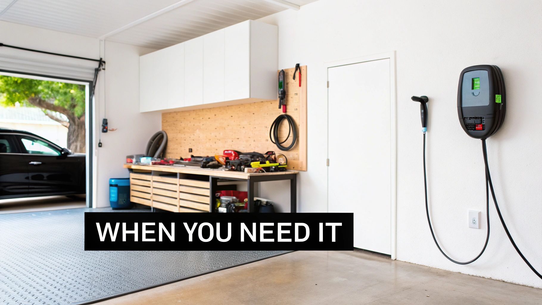 A modern, well-equipped garage featuring an electric vehicle charging station, workbench, and car outside.