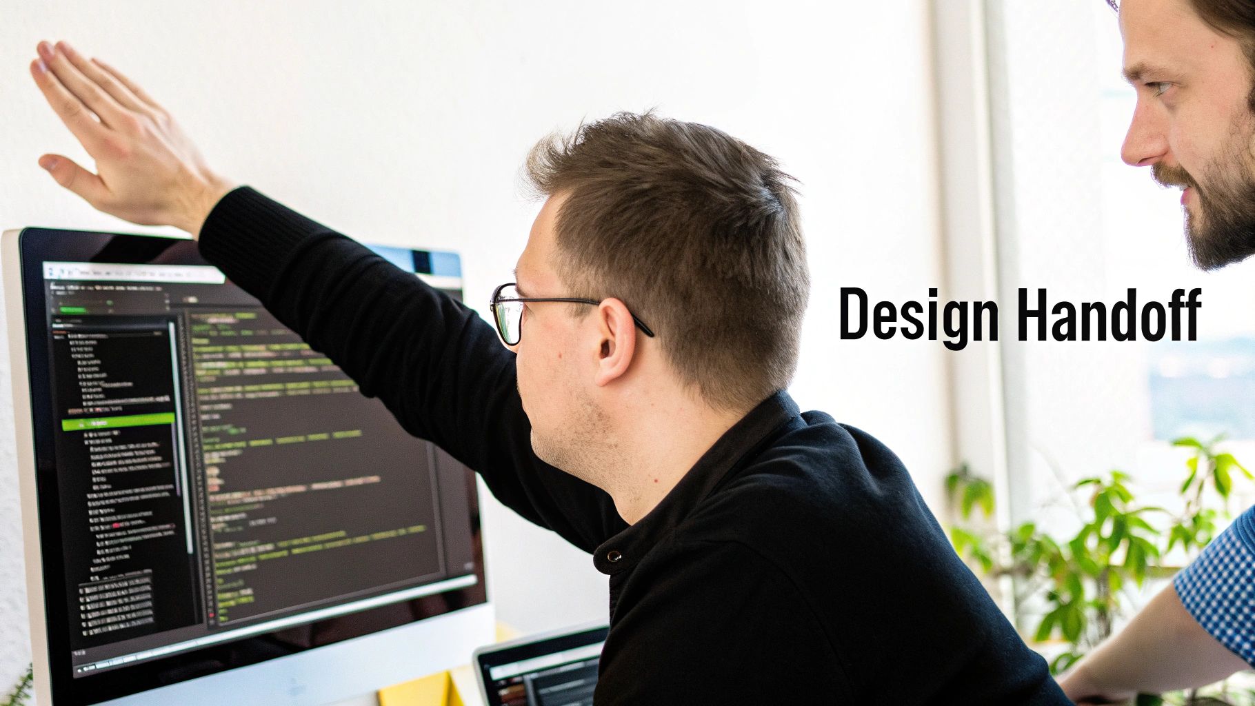 Two software developers discuss code on a computer screen, indicating a design handoff.