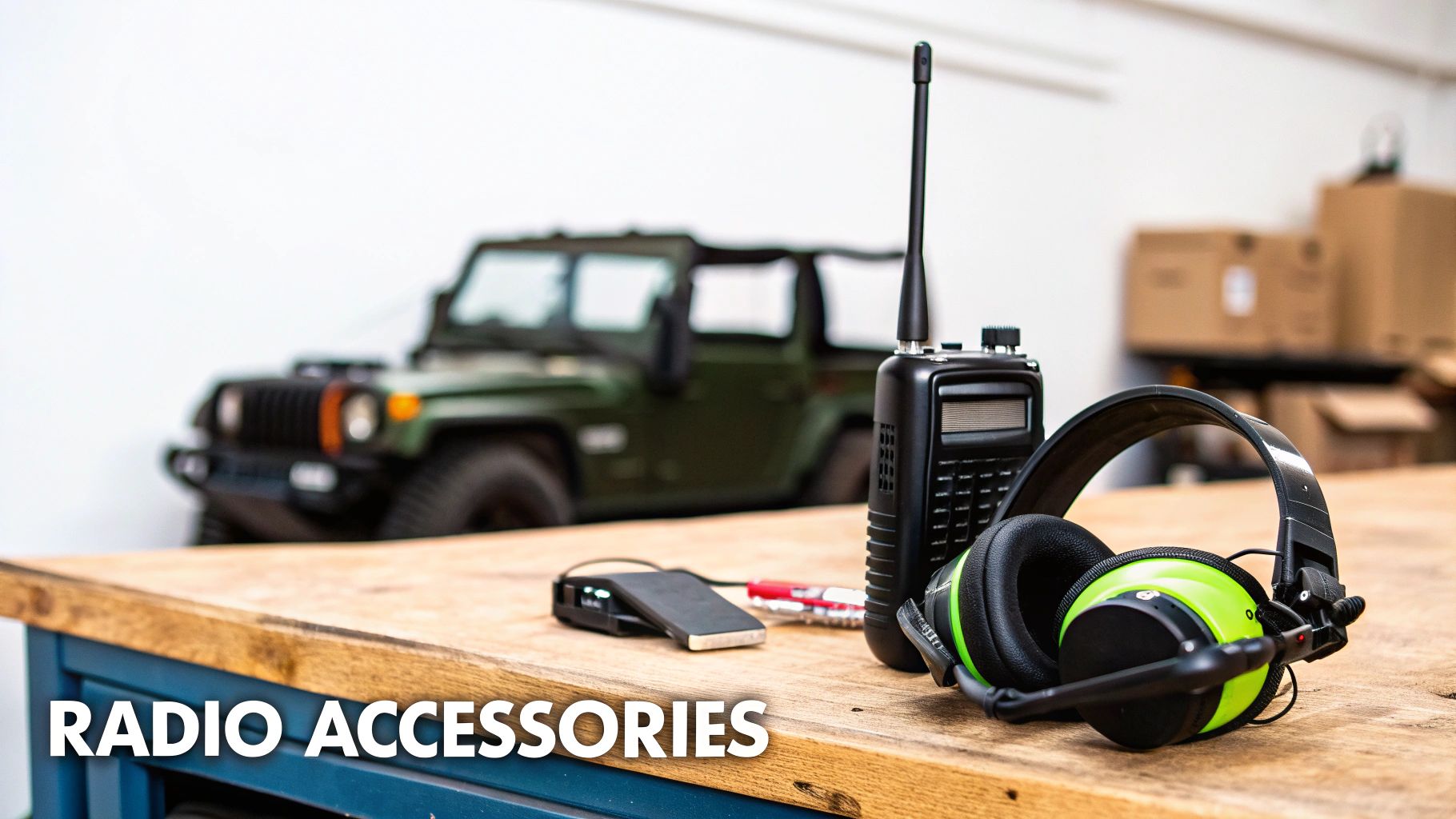 A walkie-talkie, headphones with microphone, and other radio accessories on a wooden table with a Jeep.