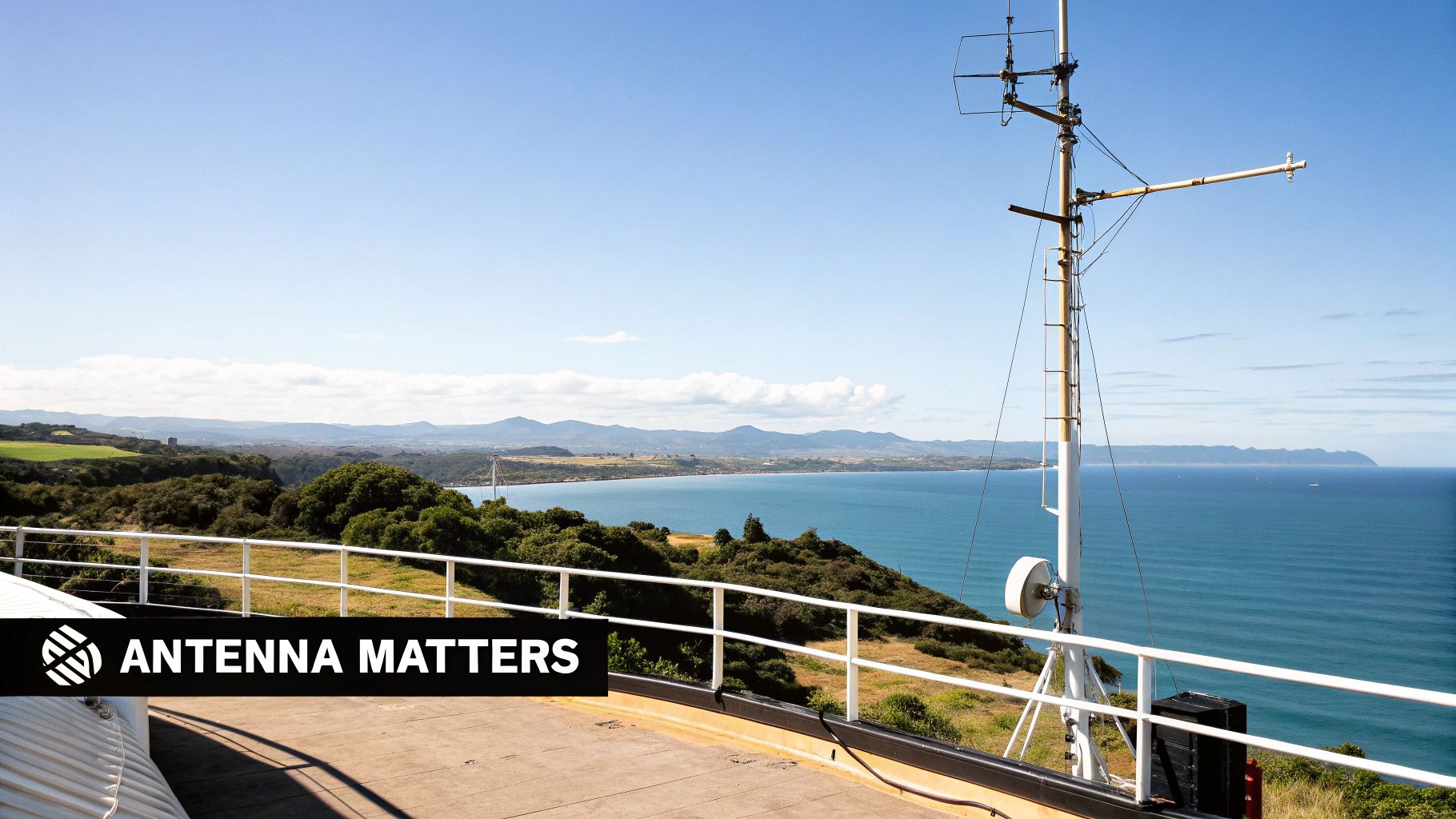 A coastal communication mast with antennas overlooking a beautiful blue ocean, coastline, and distant mountains.