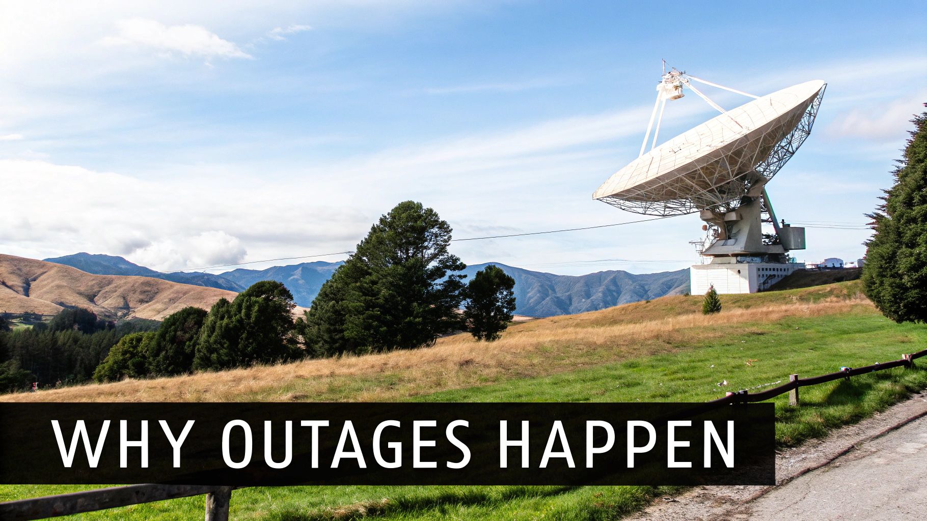 A large satellite dish stands prominently on a grassy hill with distant mountains under a blue sky.