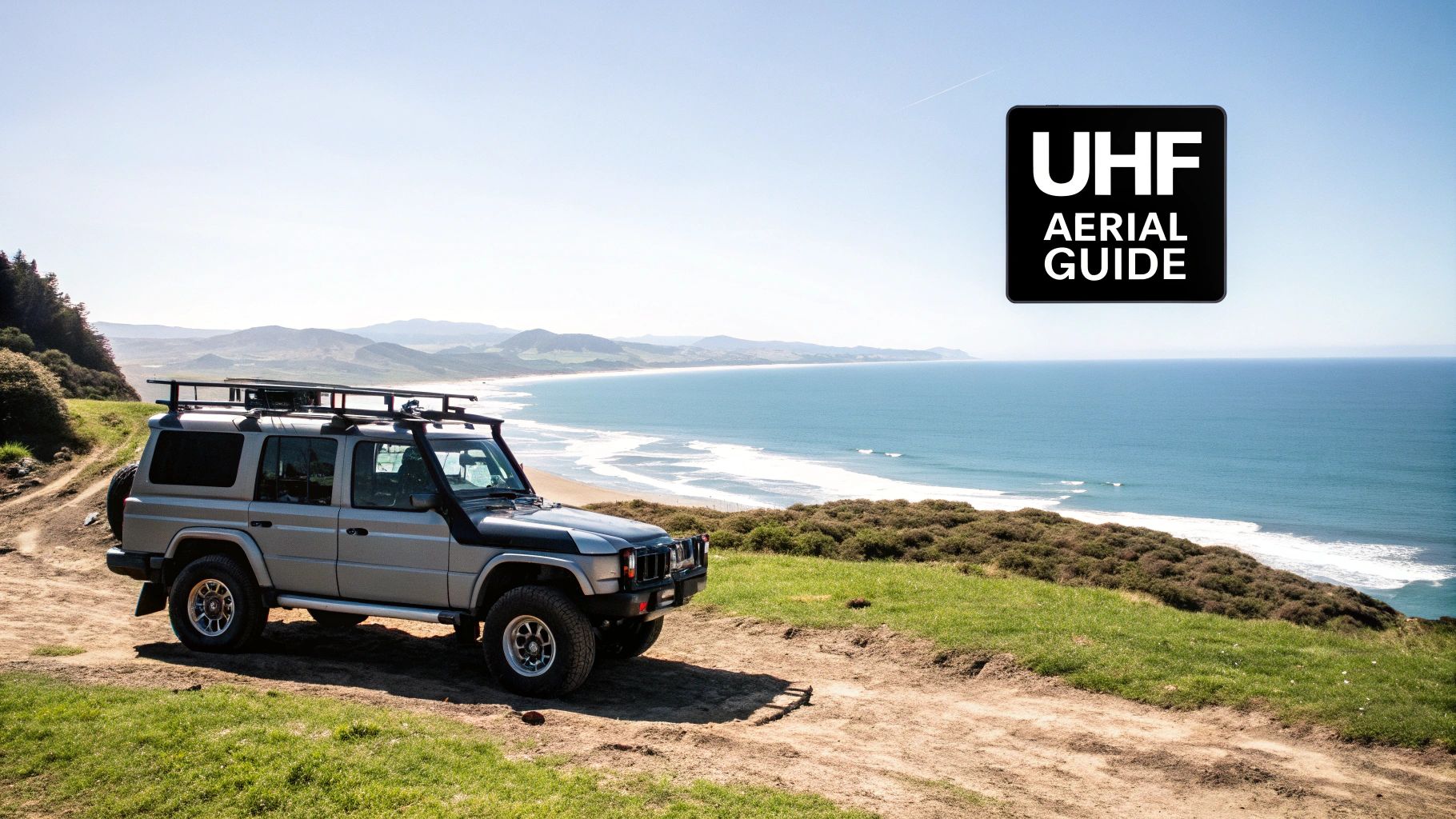 A silver 4x4 SUV parked on a coastal dirt track overlooking a scenic beach and ocean.