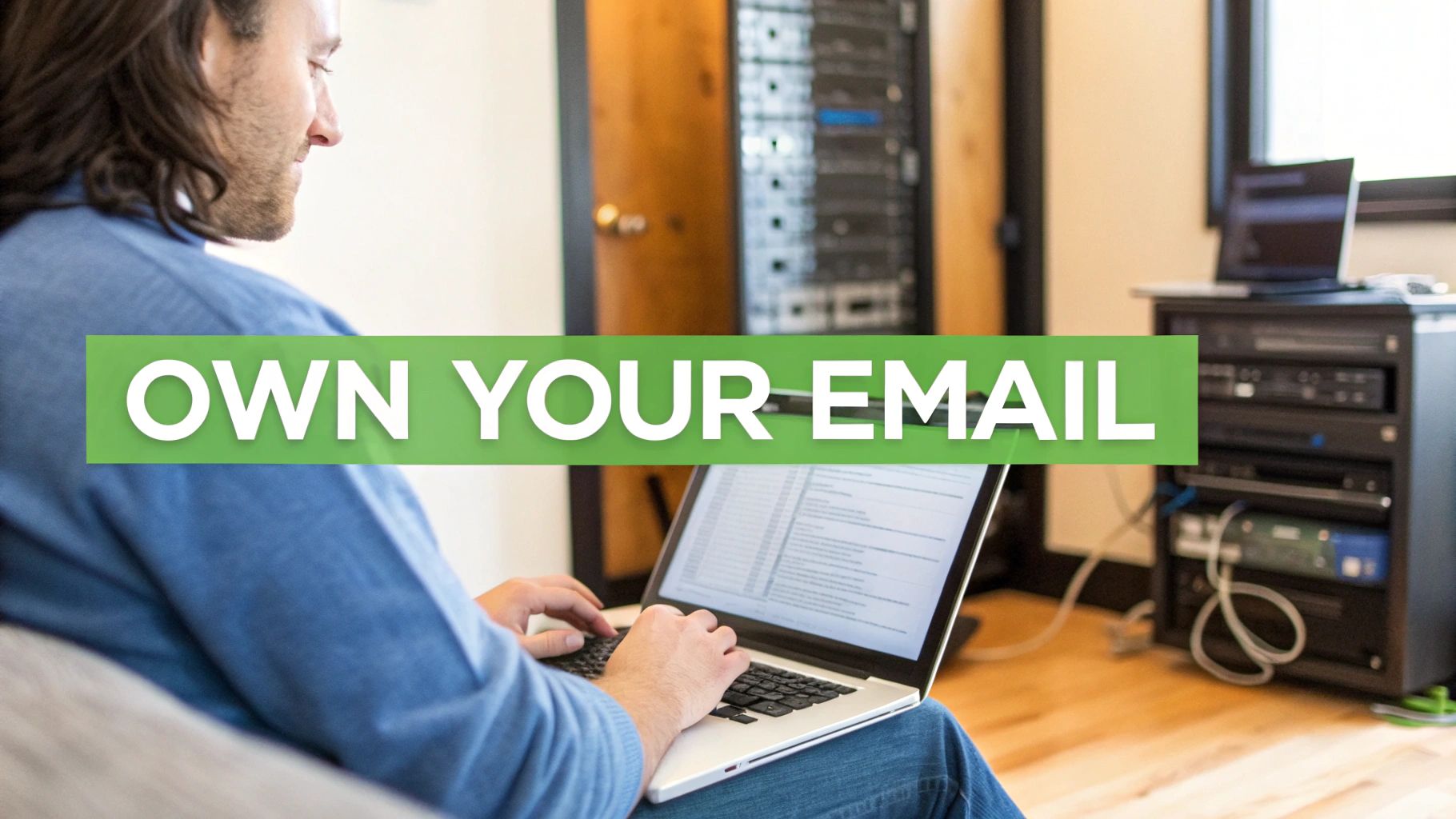 A man types on a laptop with an "OWN YOUR EMAIL" banner, near a server rack.