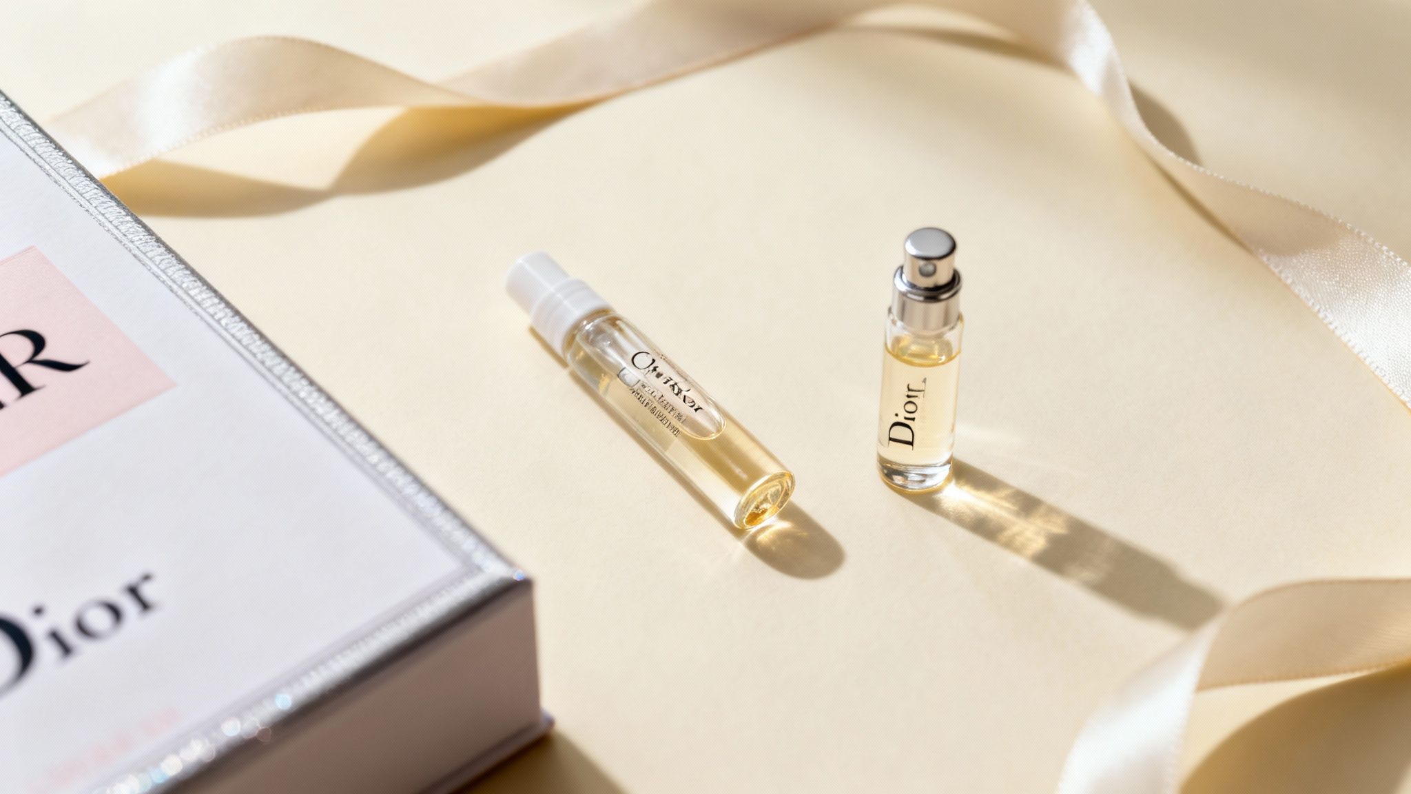 Two Christian Dior perfume samples with a branded box and ribbon on a light background.