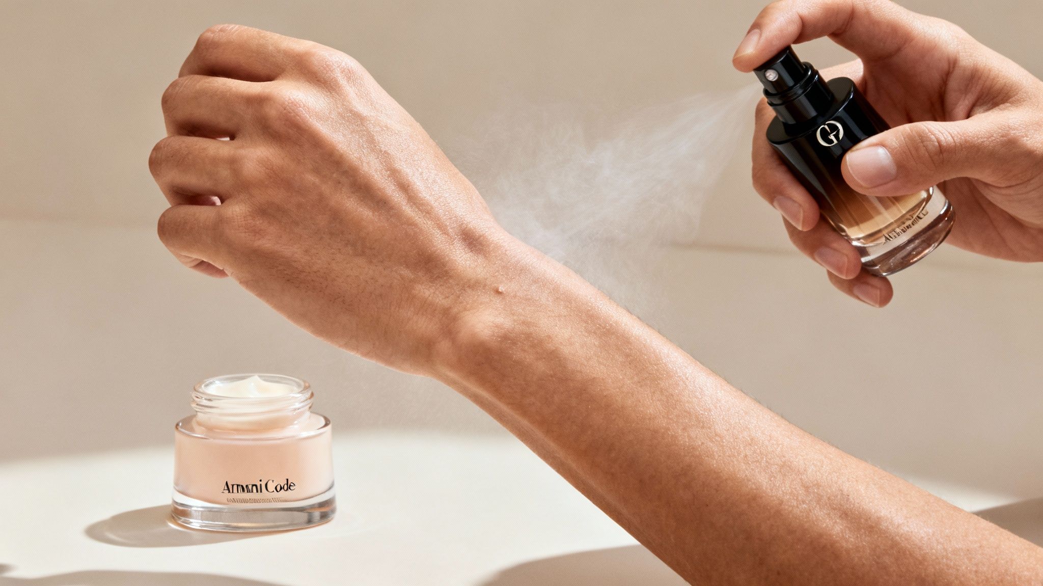 A person's arm is sprayed with fragrance from a bottle, with an Armani Code cream jar nearby.