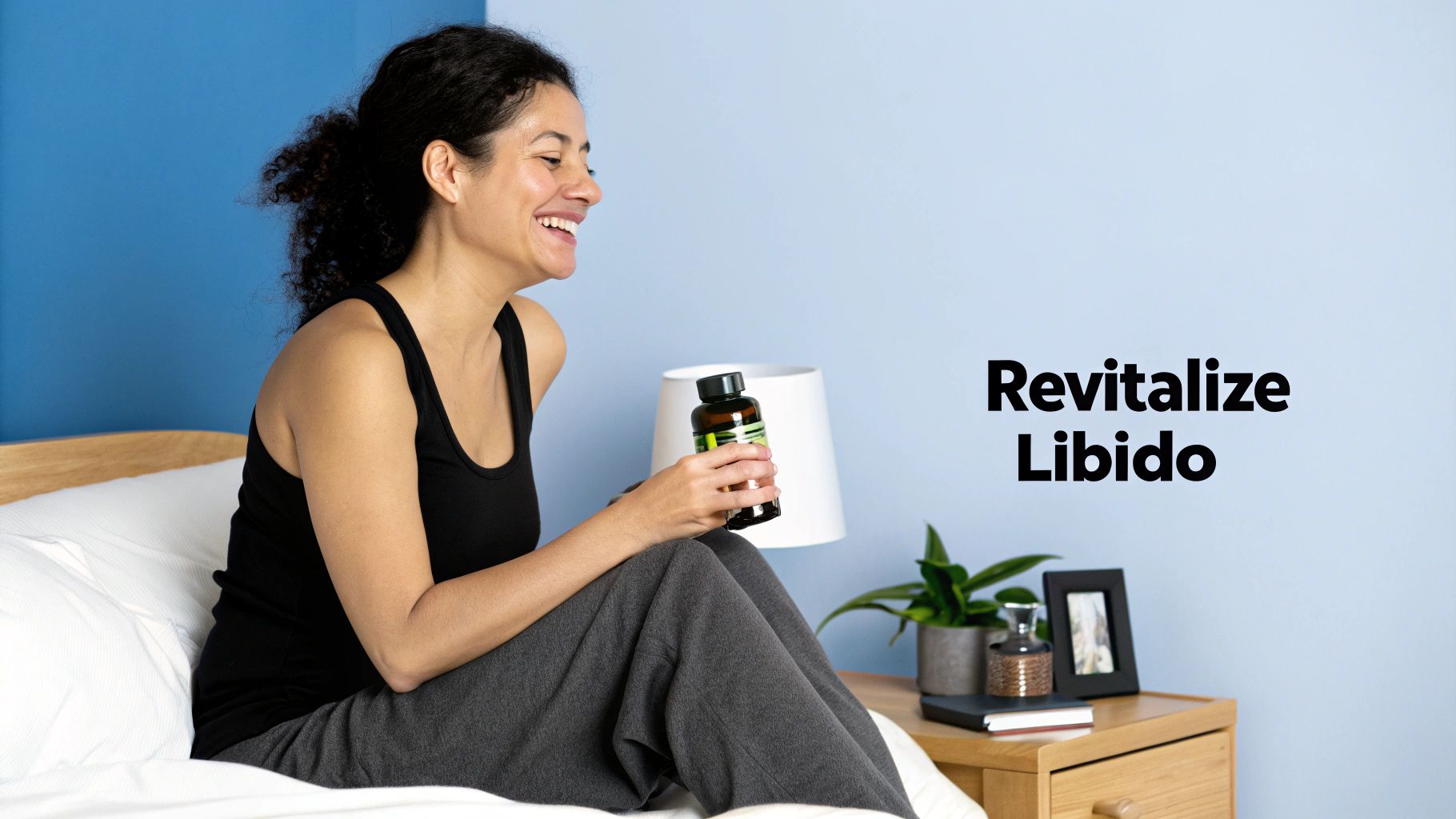A happy woman sits on a bed, smiling and holding a bottle of libido revitalizing supplement.