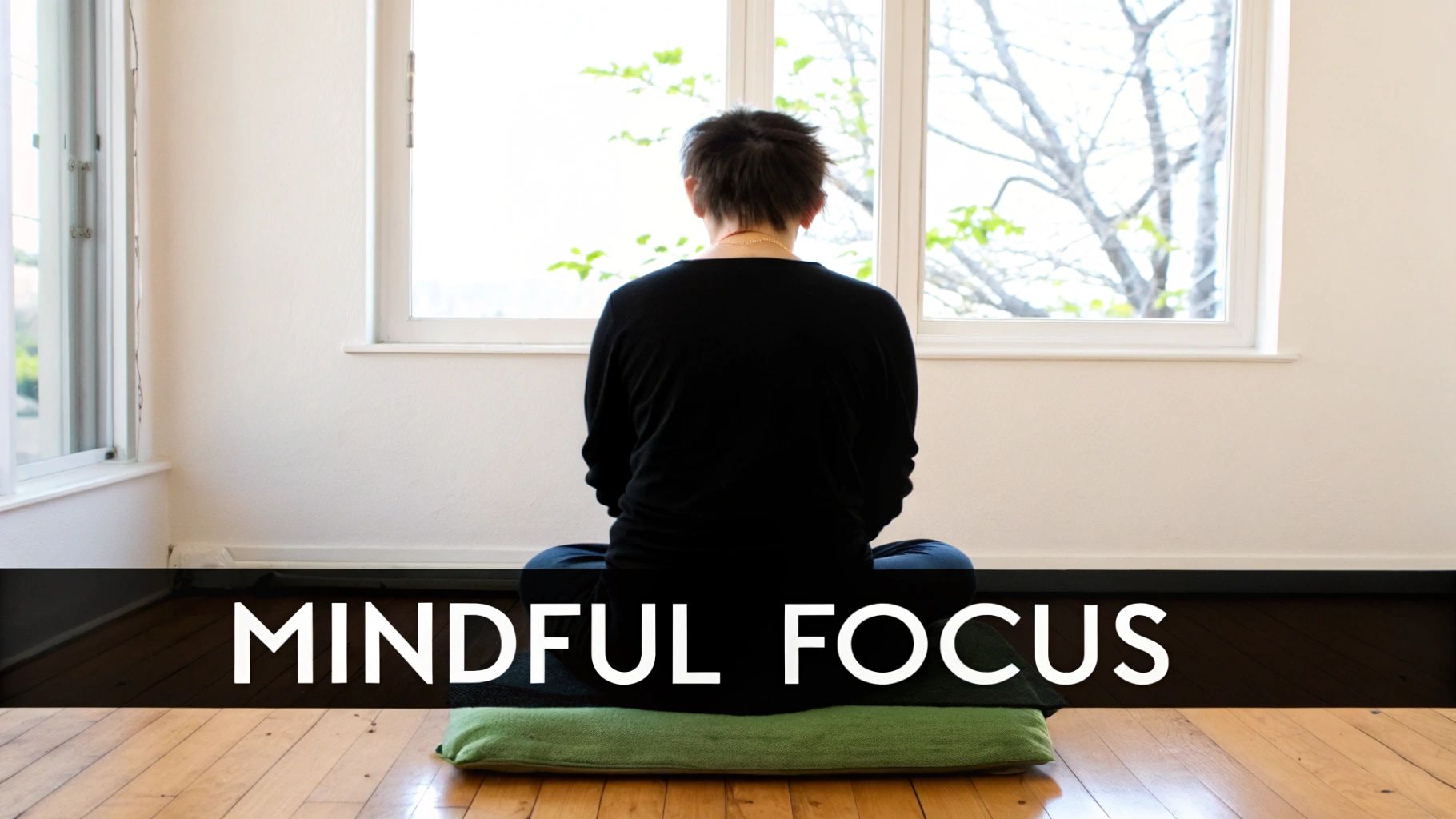 A person with short hair meditating on a cushion, facing a bright window with trees.