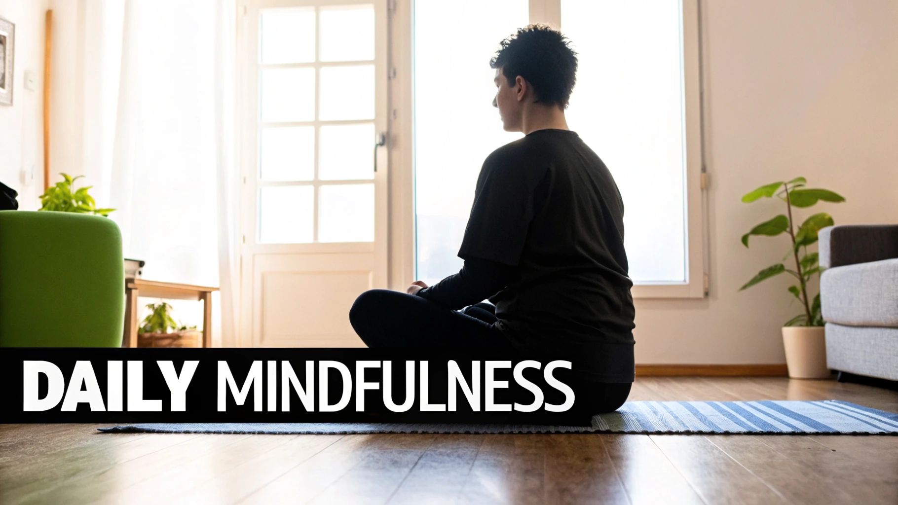 A person in black attire sits meditating on a blue striped yoga mat in a sunlit room.
