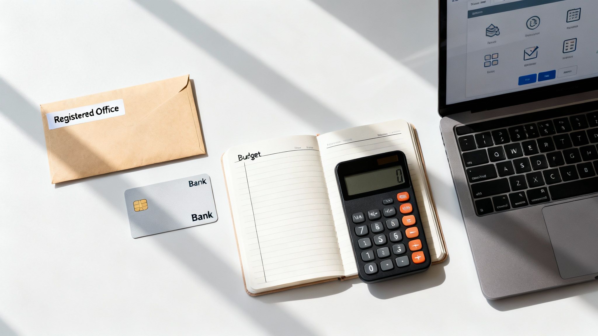 A flat lay of a desk with an envelope, credit card, budget notebook, calculator, and laptop.