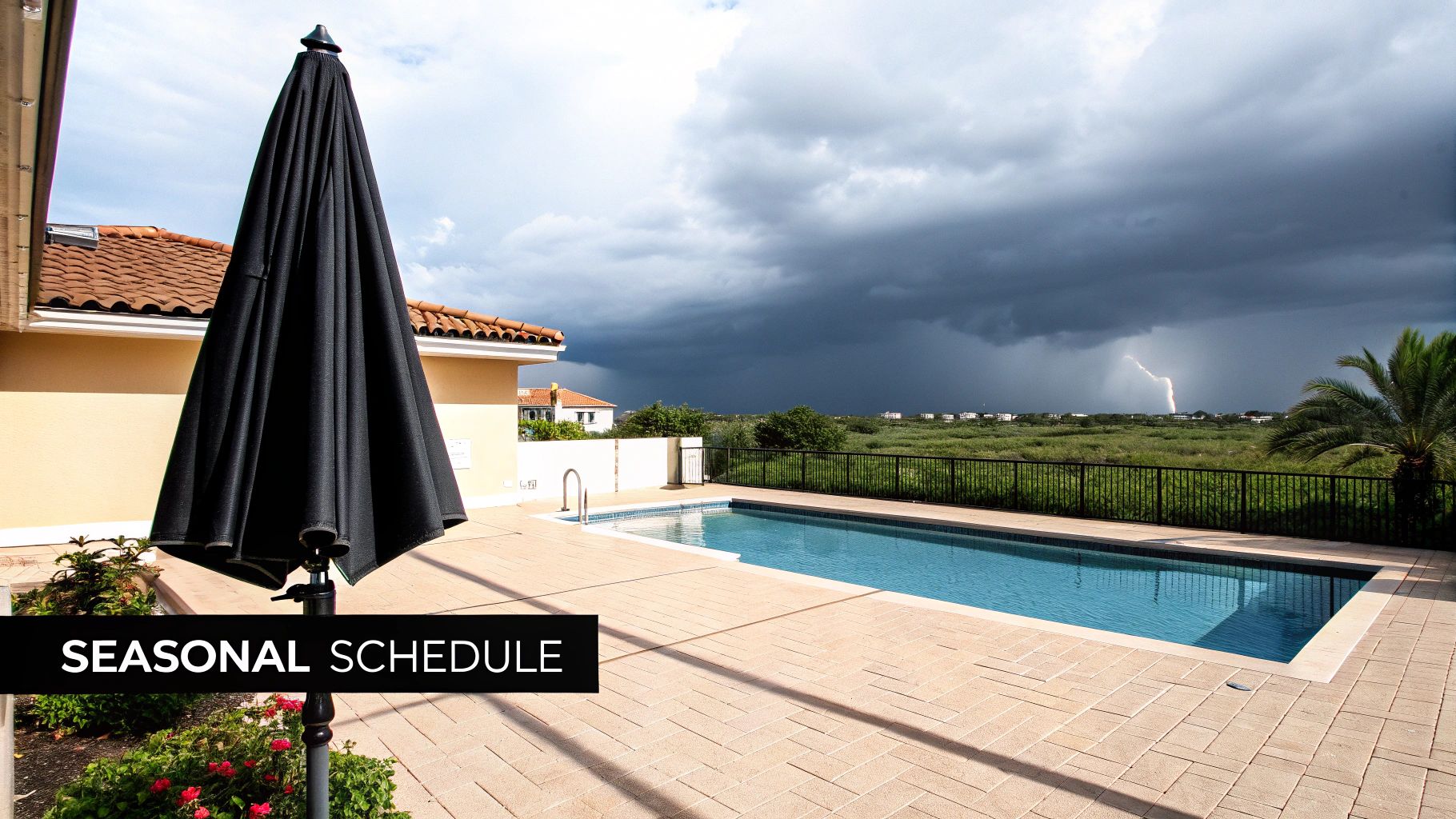 A backyard swimming pool with a black umbrella and a distant lightning strike under a stormy sky.