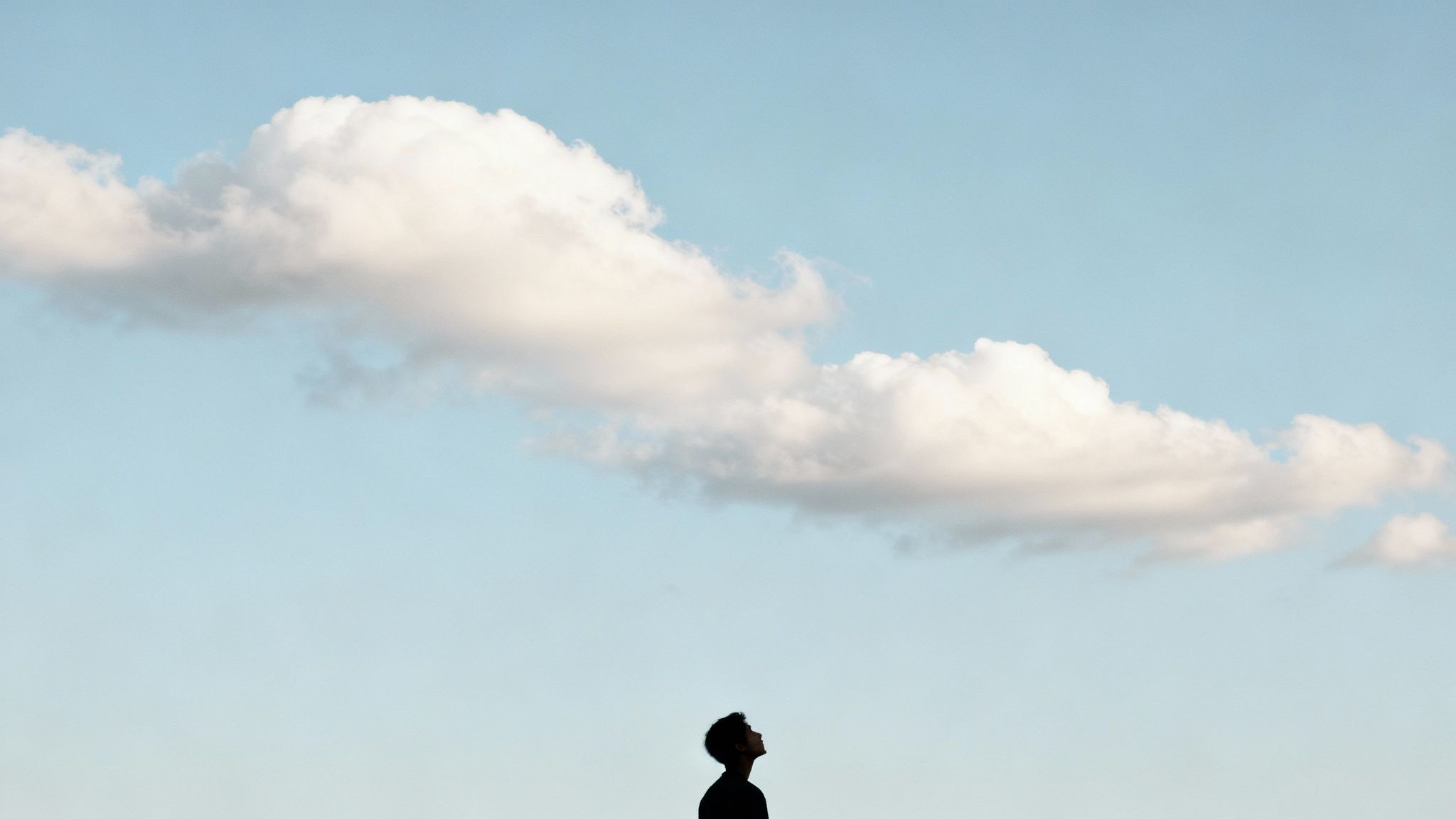 Un homme en silhouette contemple un nuage solitaire dans un vaste ciel bleu, symbolisant la pleine conscience.