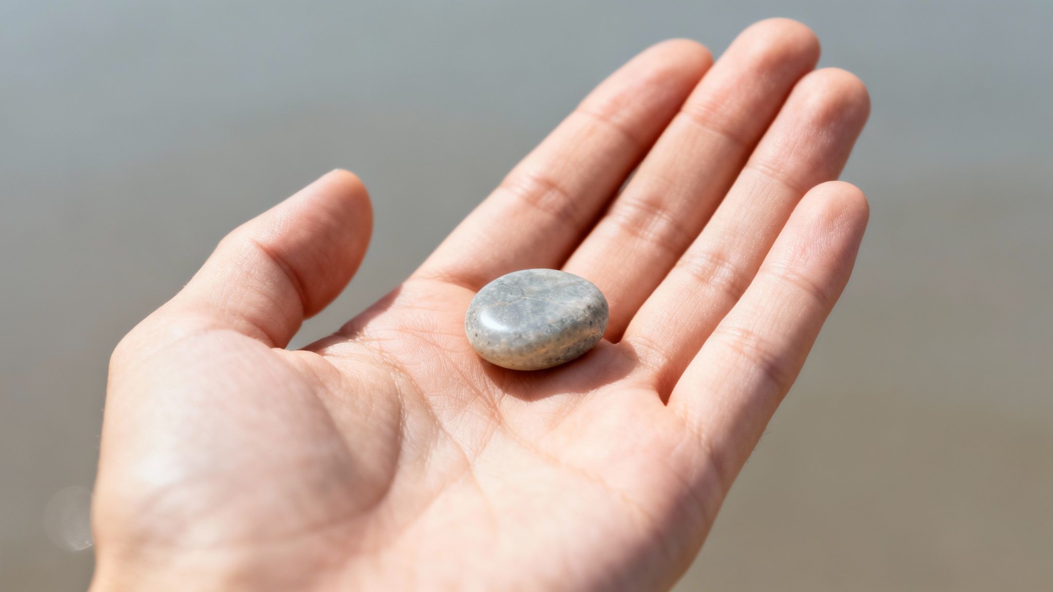 Une main tient délicatement une pierre lisse et grise au creux de sa paume, sur un fond clair et flou.