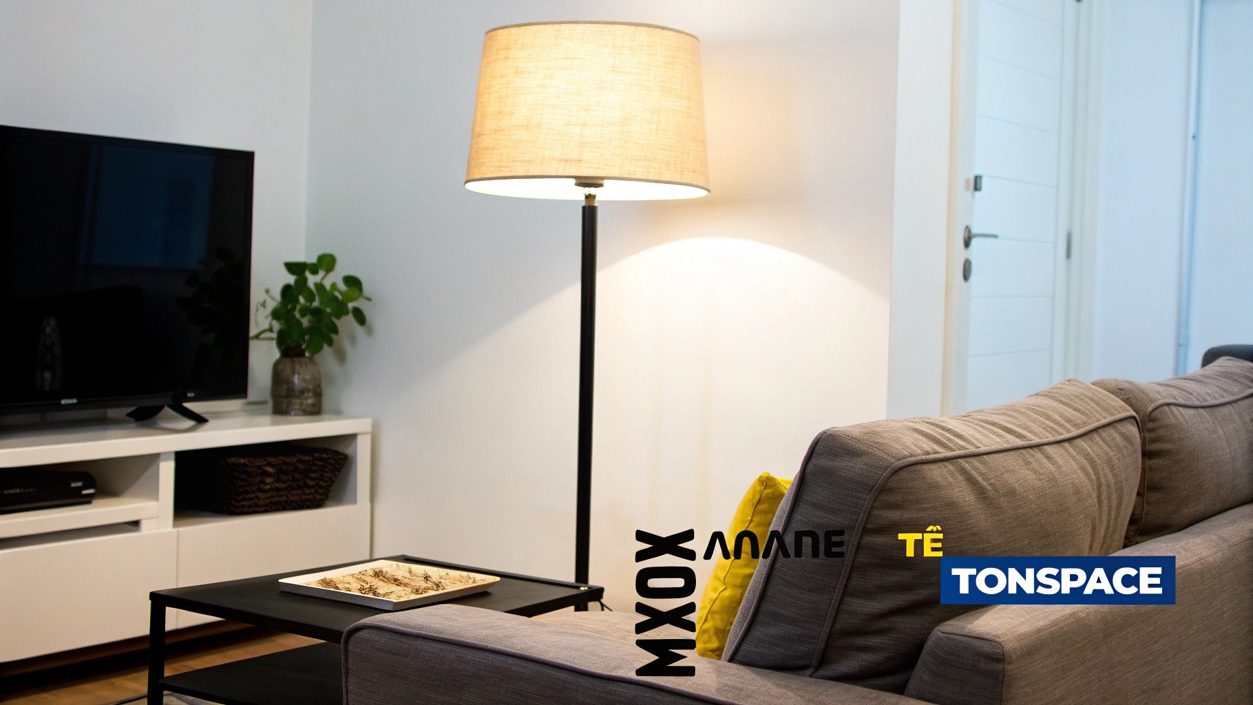 Ένα άνετο σαλόνι με φωτιστικό δαπέδου, γκρι καναπέ, τηλεόραση και φυτό.