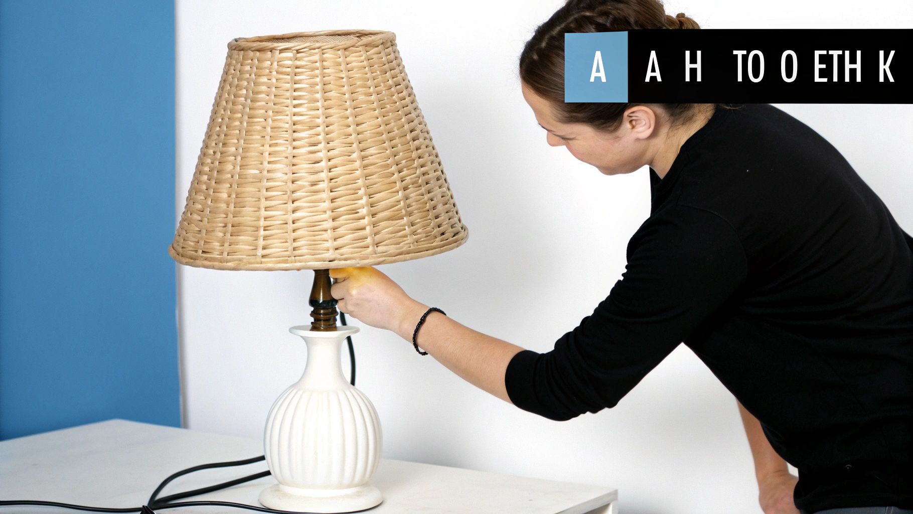 Γυναίκα ανάβει ένα φωτιστικό με ψάθινο καπέλο και λευκή βάση σε τραπέζι.