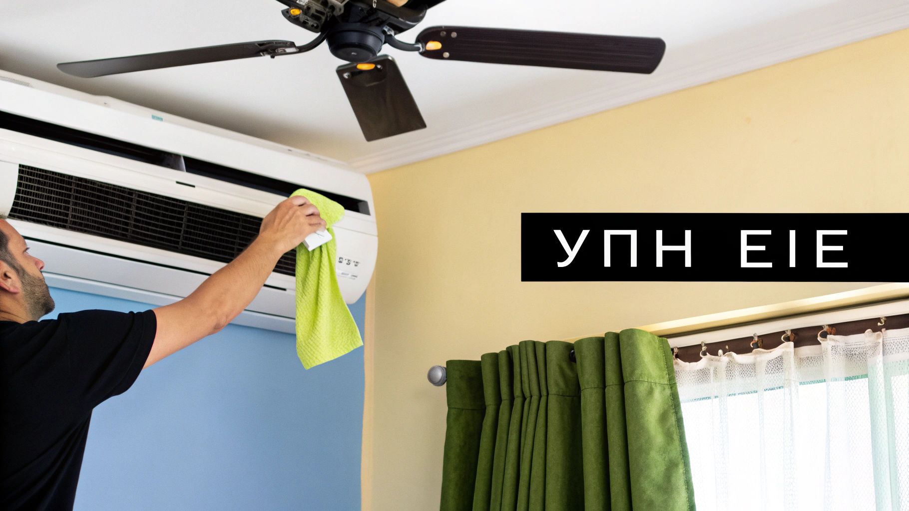 Άντρας καθαρίζει κλιματιστικό με πράσινο πανί, με ανεμιστήρα οροφής και κουρτίνες στο φόντο.