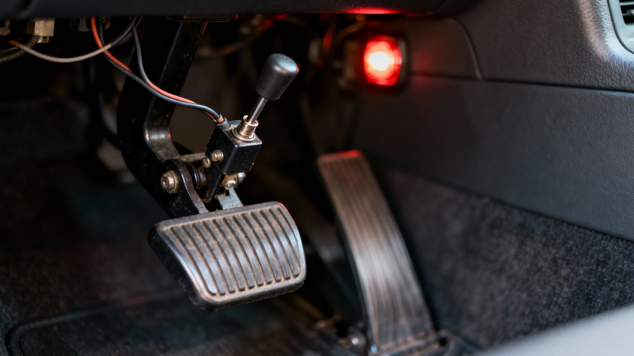A technician inspecting the brake pedal area of a car, where the brake pedal is located.