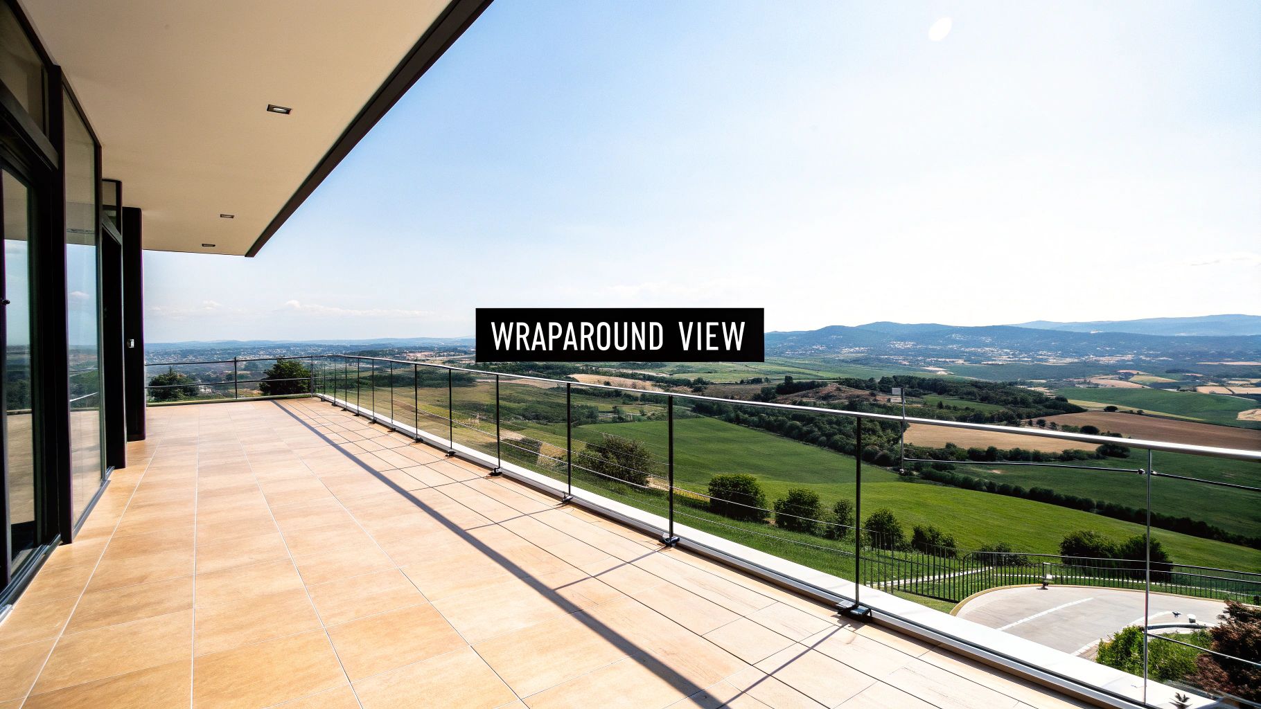 Expansive outdoor balcony with light tiles and a glass railing, showcasing a wide natural landscape.