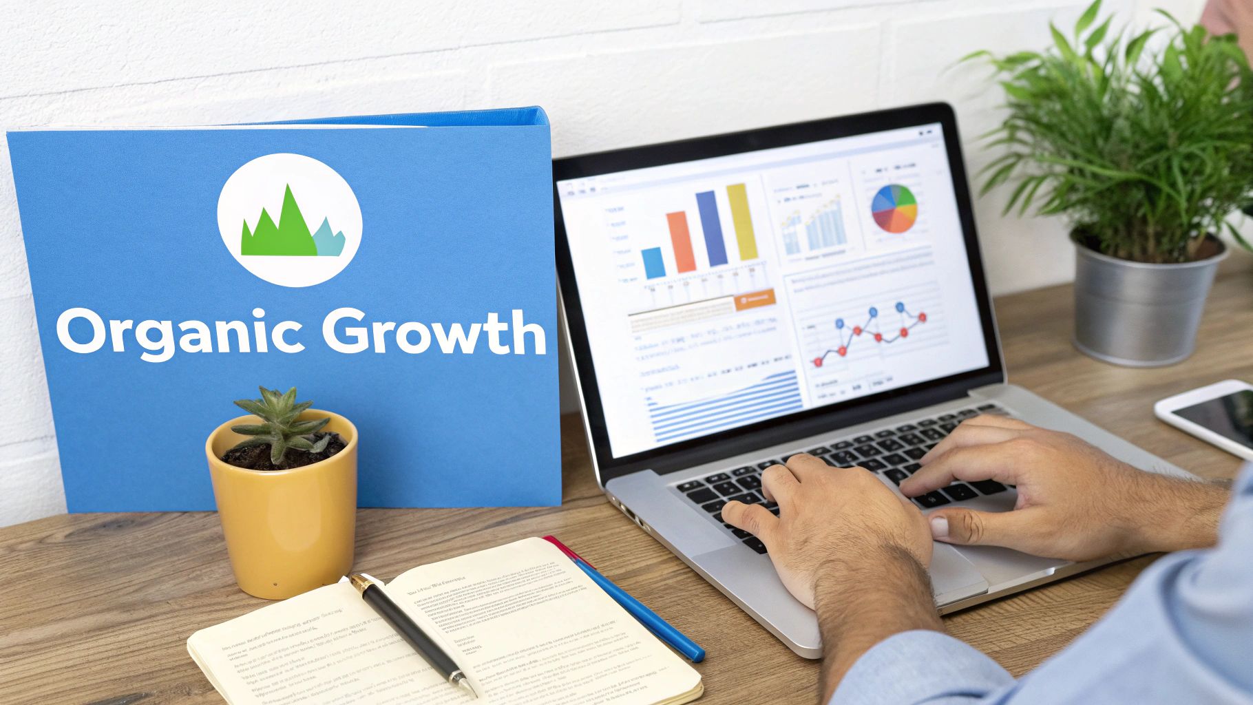 Person analyzing business data on a laptop, next to an 'Organic Growth' binder, plants, and notebook.
