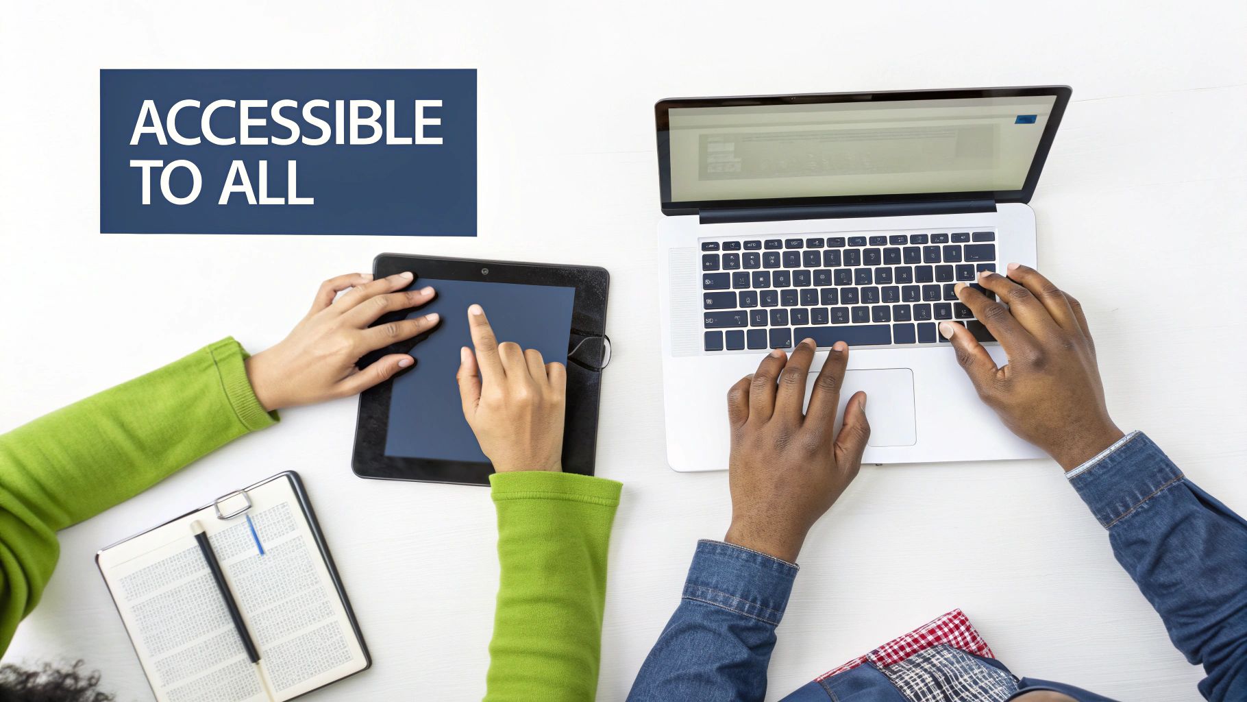 Two people are using a tablet and a laptop on a white desk with a sign 'Accessible to all'.