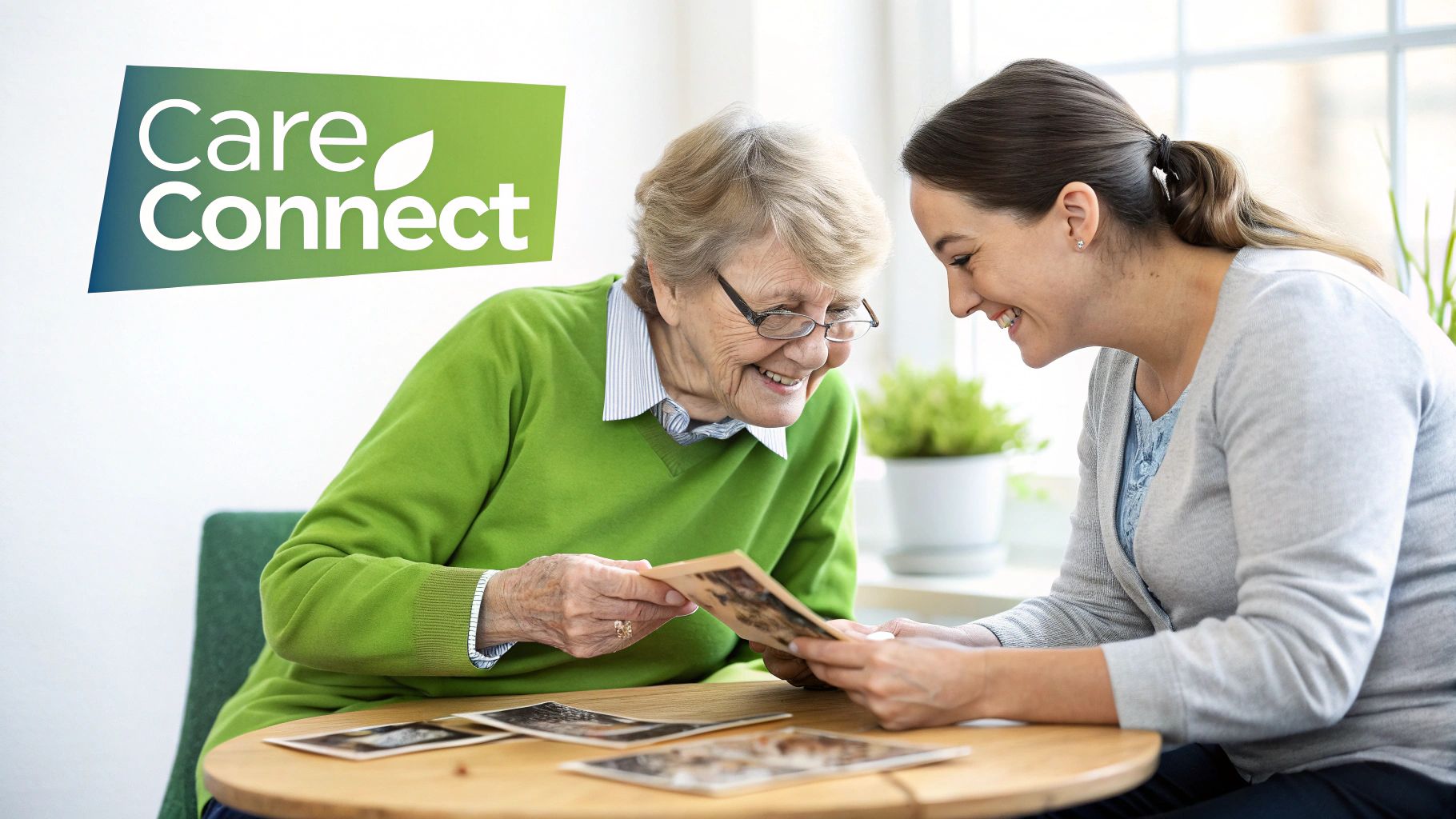 Two smiling women, an elderly woman and a younger caregiver, looking at old photos together.