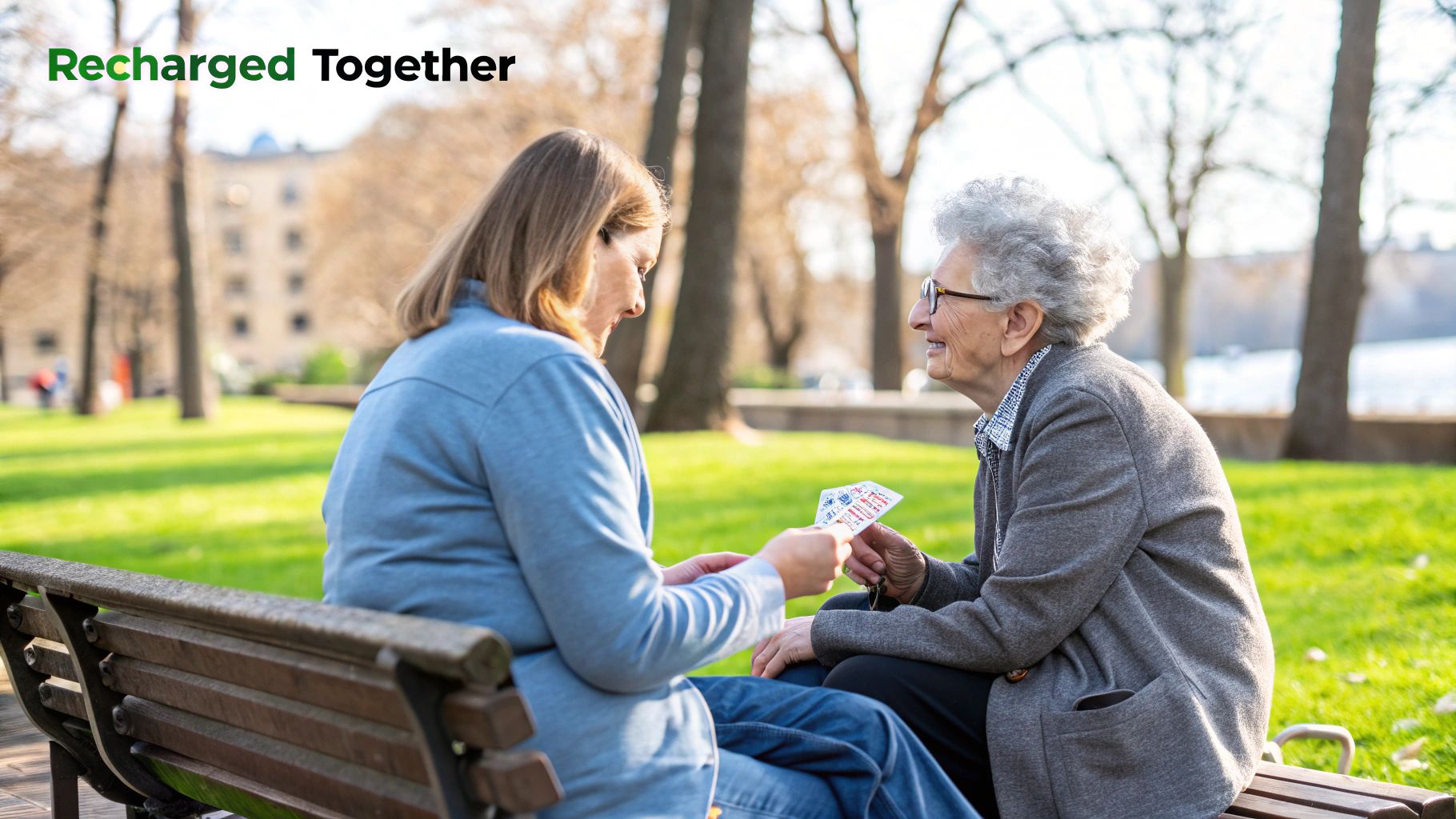 Two women, one younger and one elderly, smile while playing cards on a park bench.