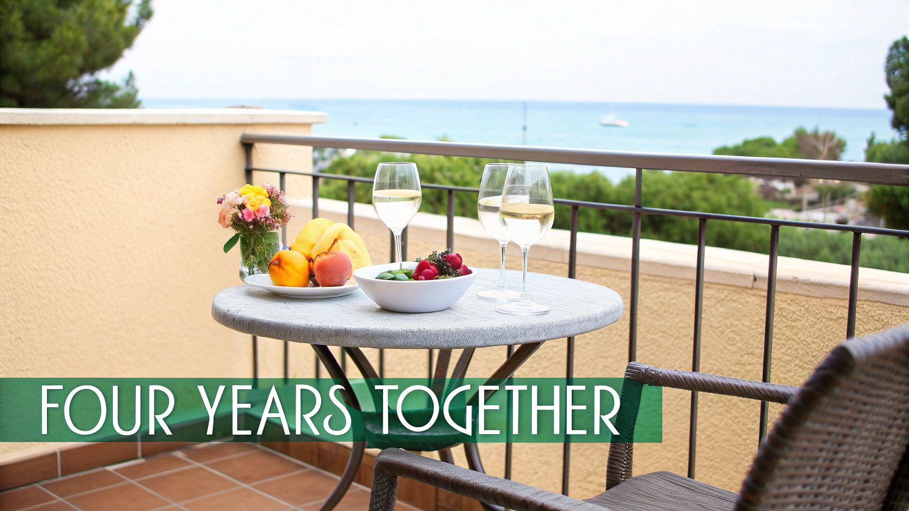 A balcony with a table set with fruits, wine, and flowers, overlooking a serene sea view.