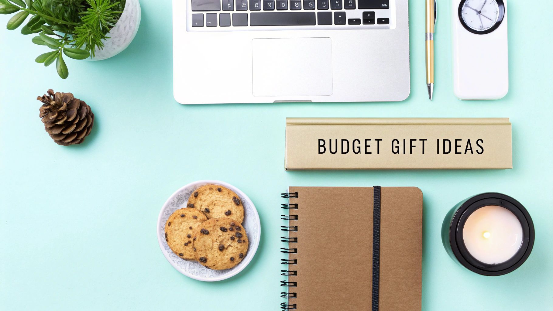 A flat lay desk setup featuring a laptop, plant, cookies, and a sign saying 'Budget Gift Ideas'.