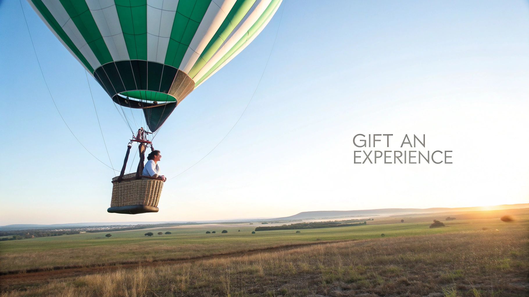 A hot air balloon with a person in the basket soaring above fields during a picturesque sunrise.