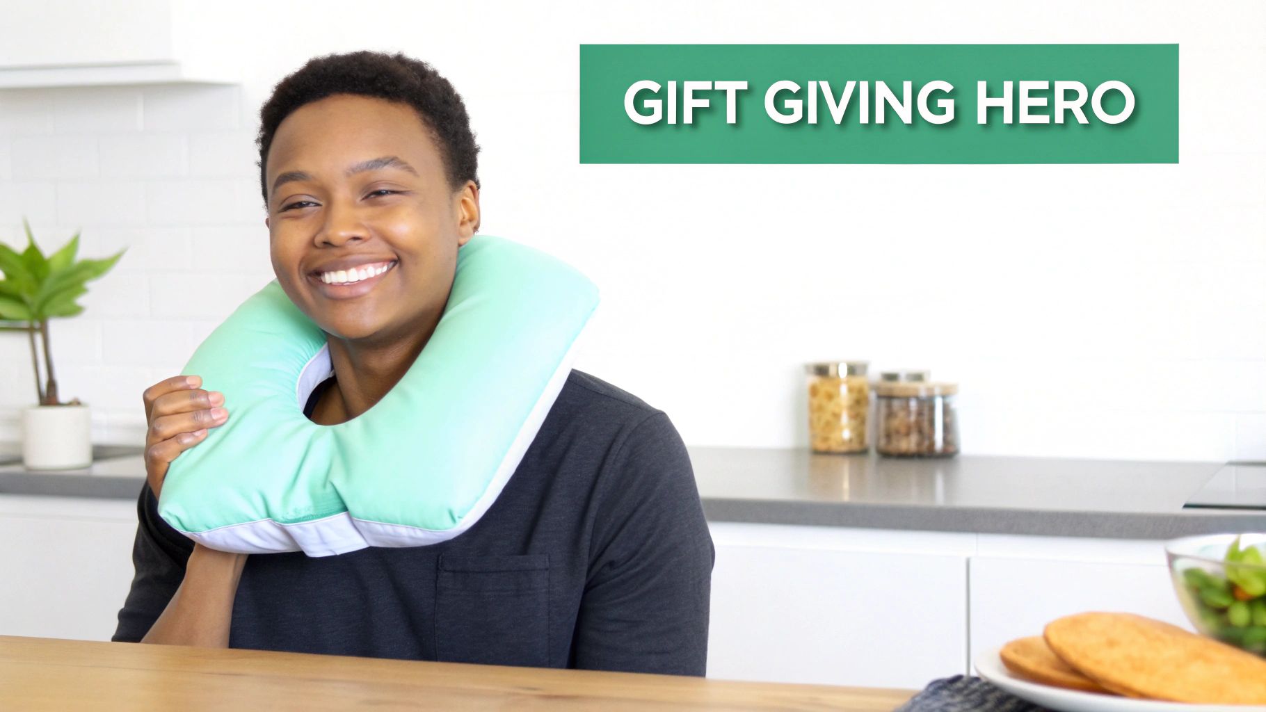 A smiling person wearing a light green U-shaped neck pillow in a modern kitchen setting.