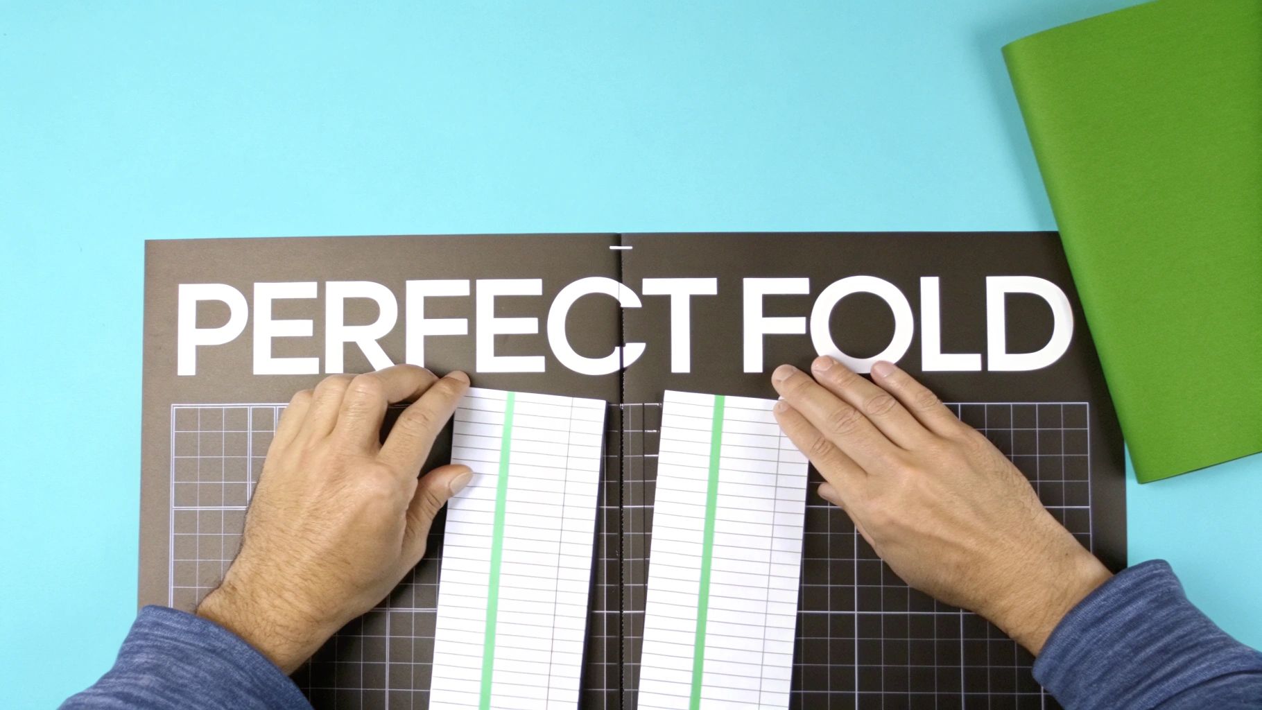A person's hands carefully align two pieces of ruled paper on a 'PERFECT FOLD' mat.