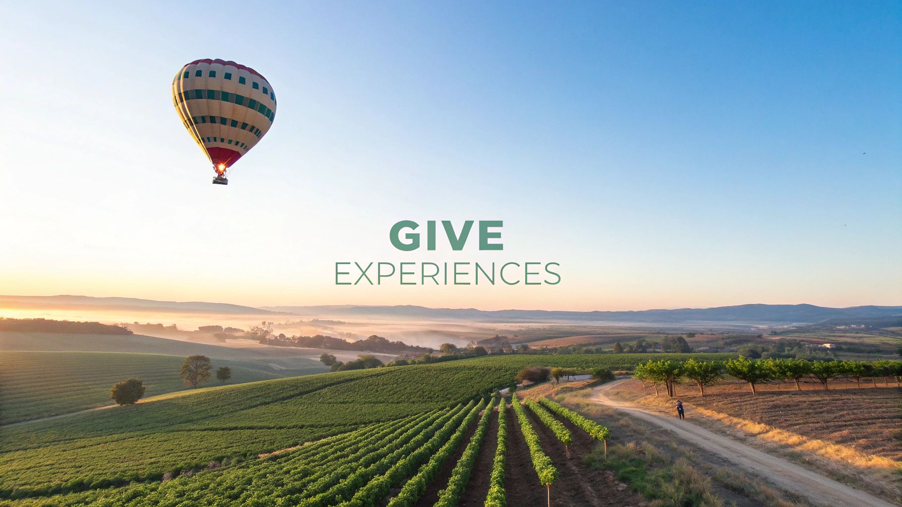A hot air balloon flying over a misty vineyard at sunrise, with 'GIVE EXPERIENCES' text.