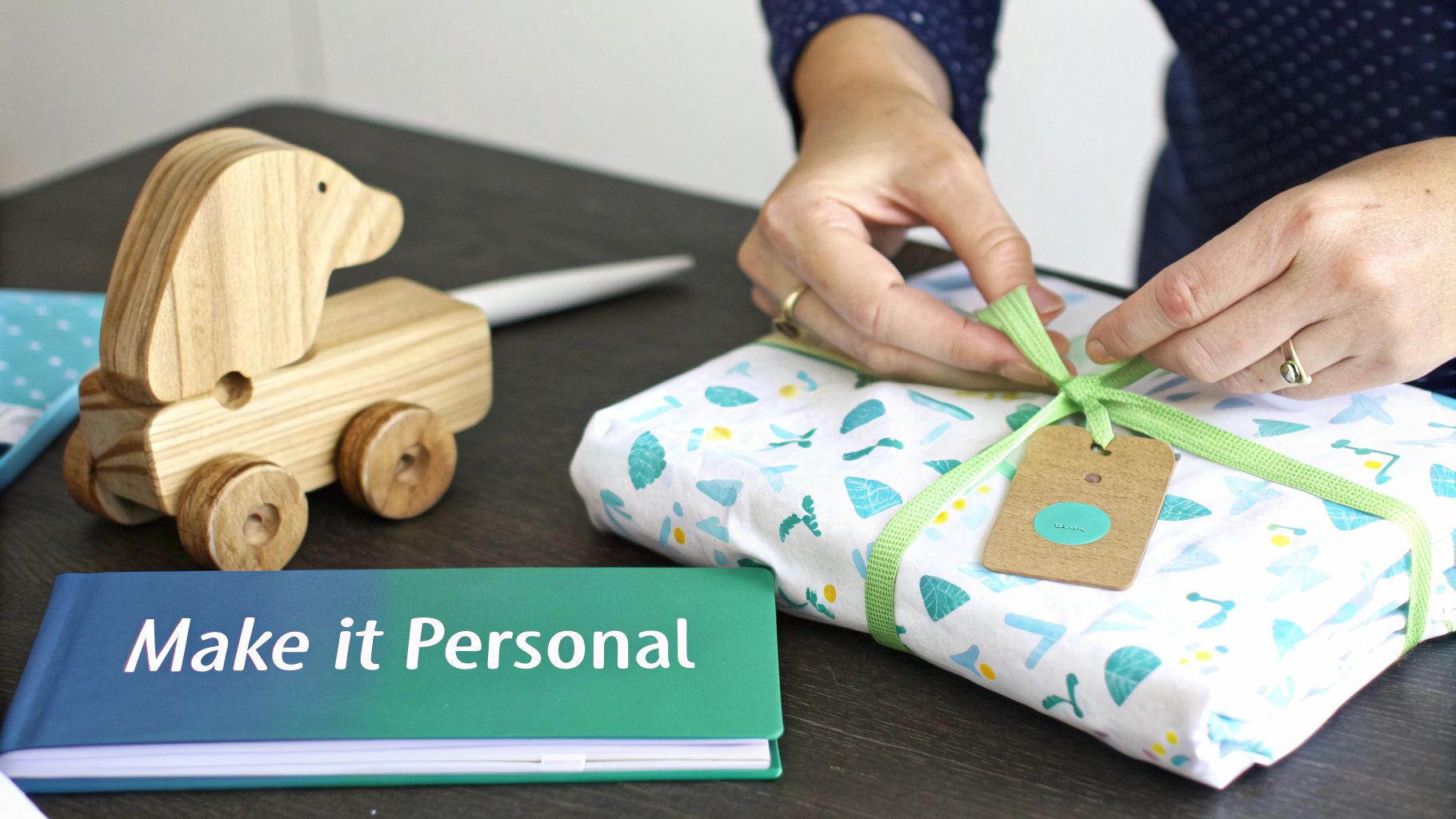 A person's hands are tying a green ribbon on a wrapped gift, with a wooden toy nearby.