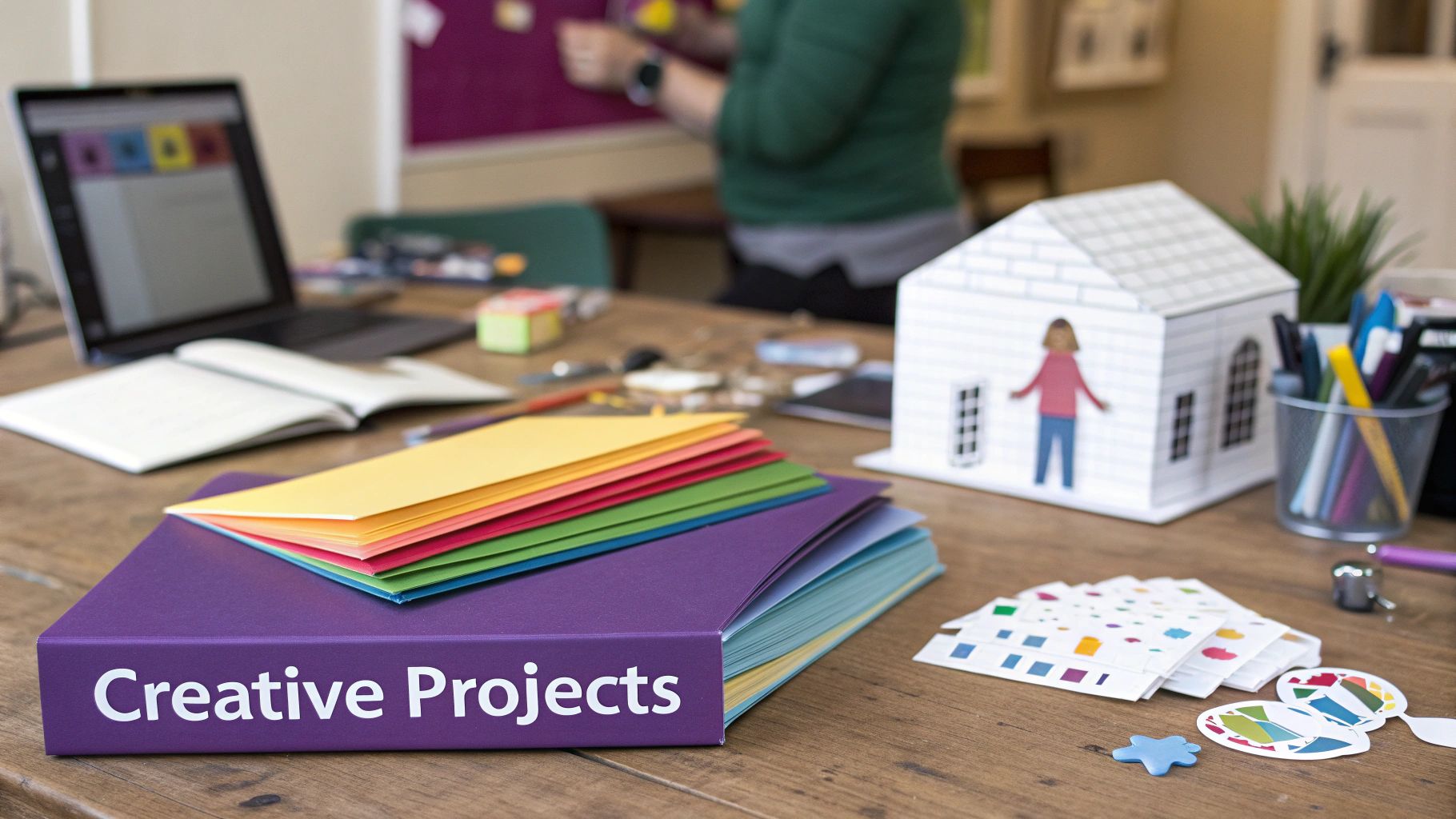 A creative workspace desk filled with craft supplies, a laptop, and a binder titled 'Creative Projects'.