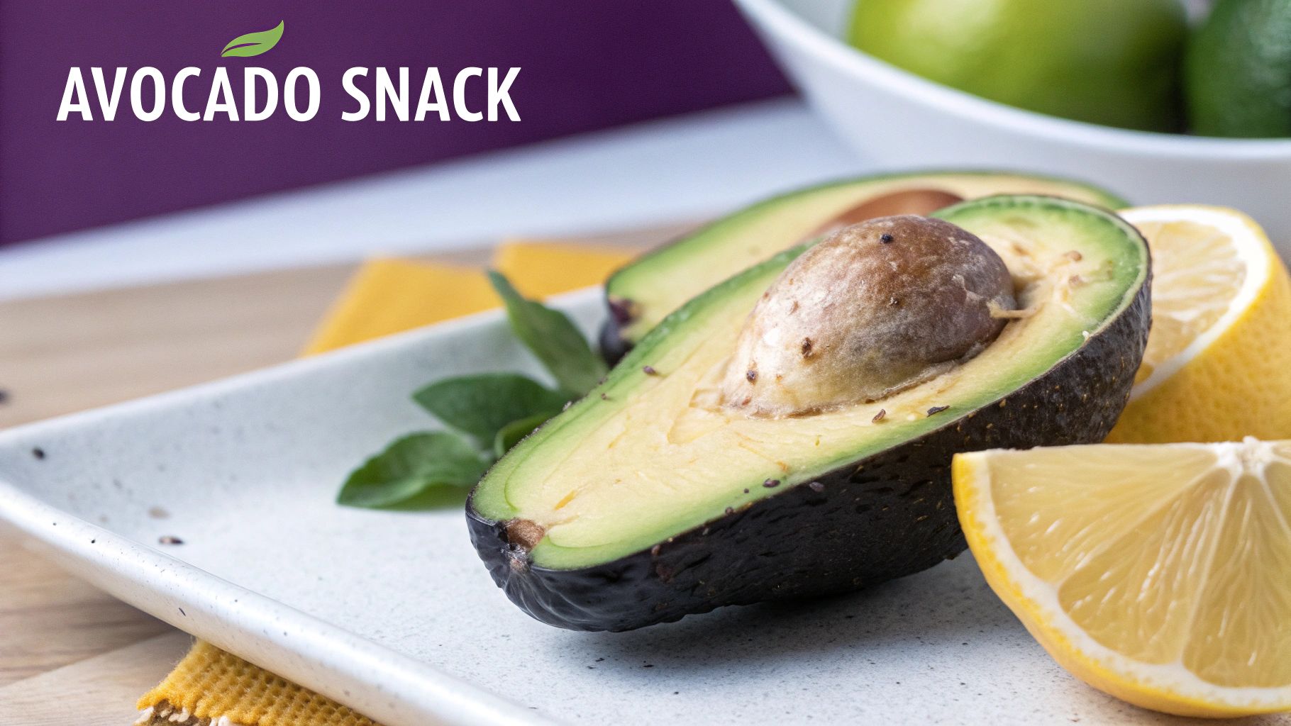 A fresh avocado halved with its pit, served on a white plate with lemon wedges and greens, labeled AVOCADO SNACK.