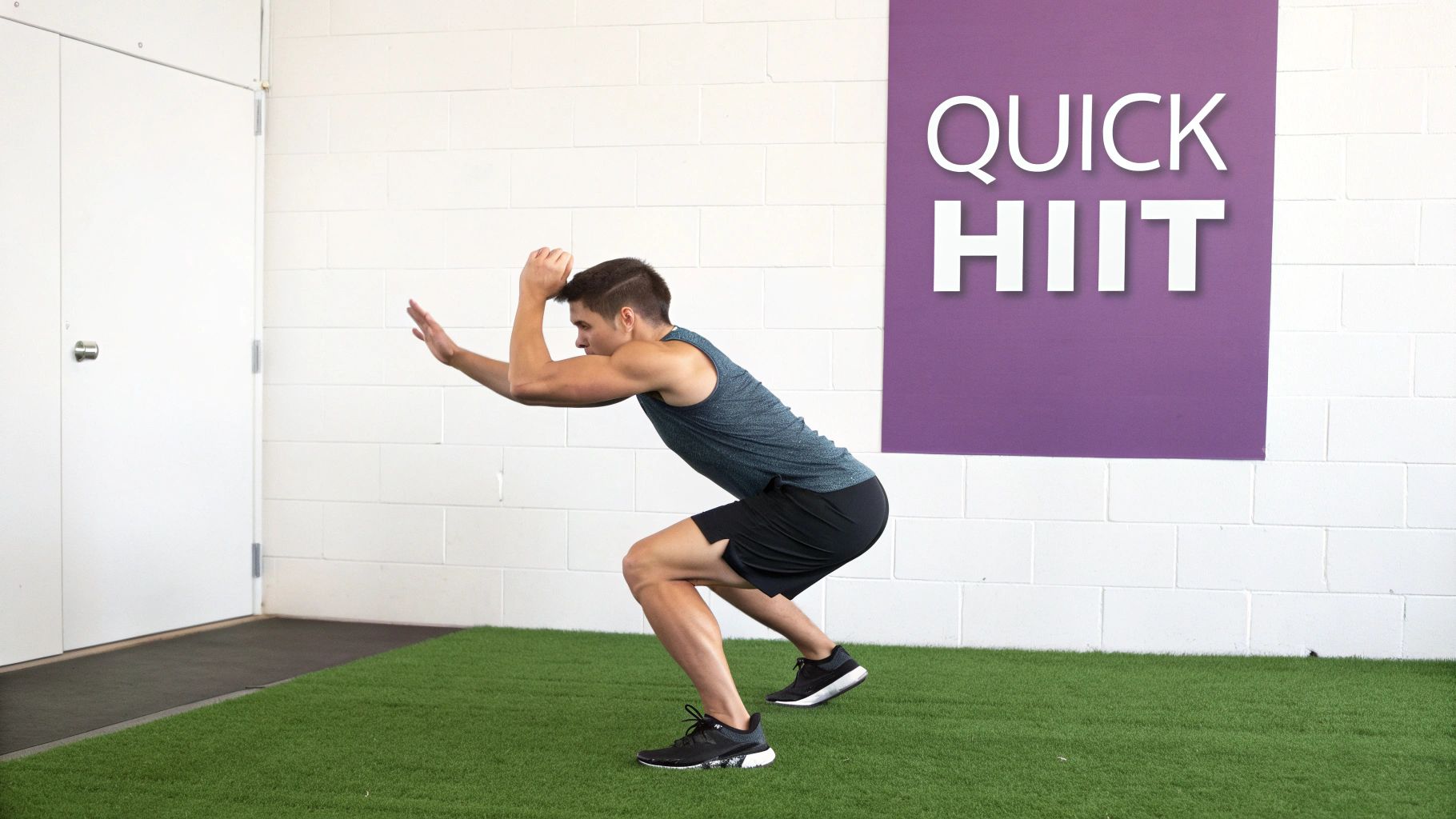 A man in athletic wear performs a squat on green turf in a modern gym setting.