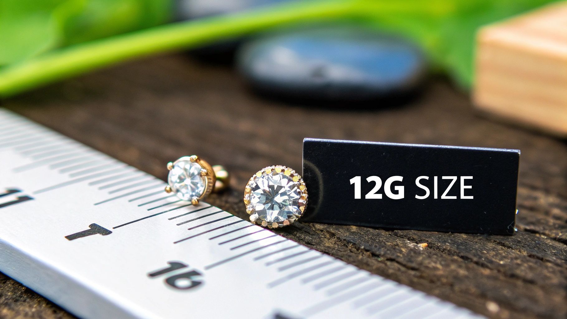 Gold-toned stud earrings with clear gemstones next to a ruler and a "12G SIZE" label on wood.