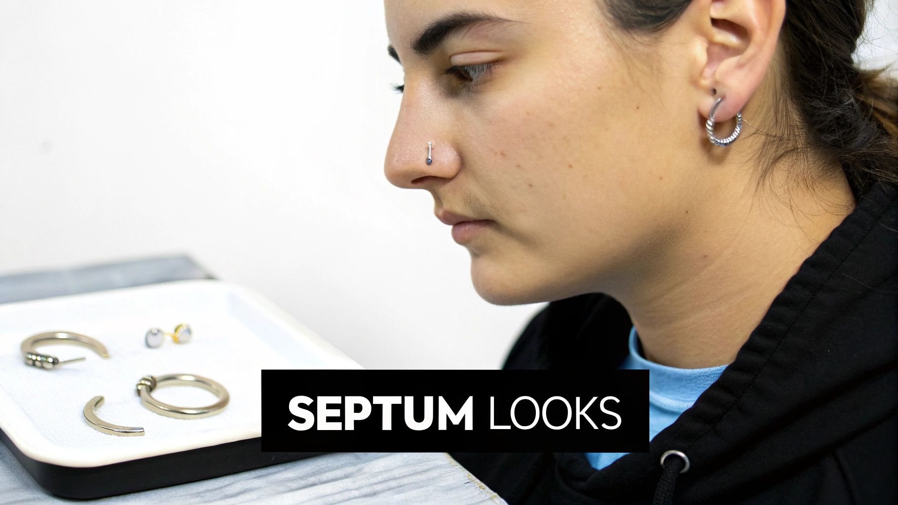 A young person with a nose piercing and ear hoop, looking at septum rings and other body jewelry.