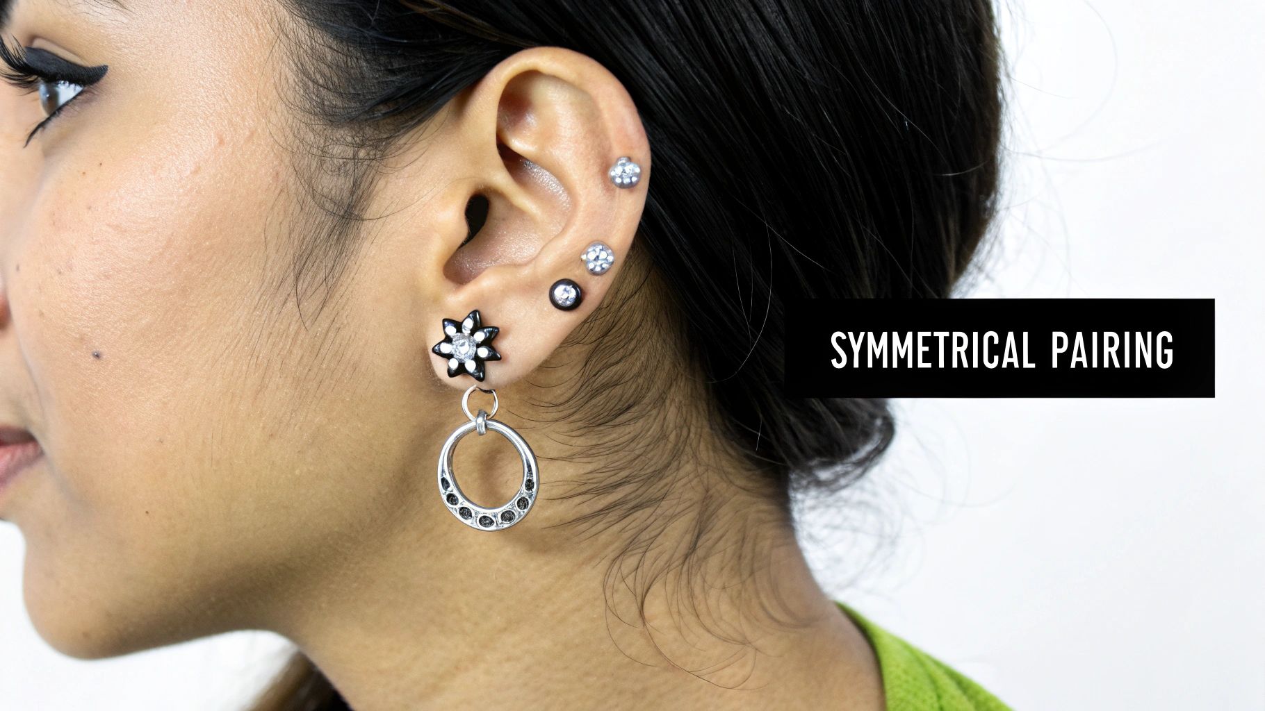 A close-up of a person's ear with multiple black and silver earrings, including a stud and a dangling hoop.