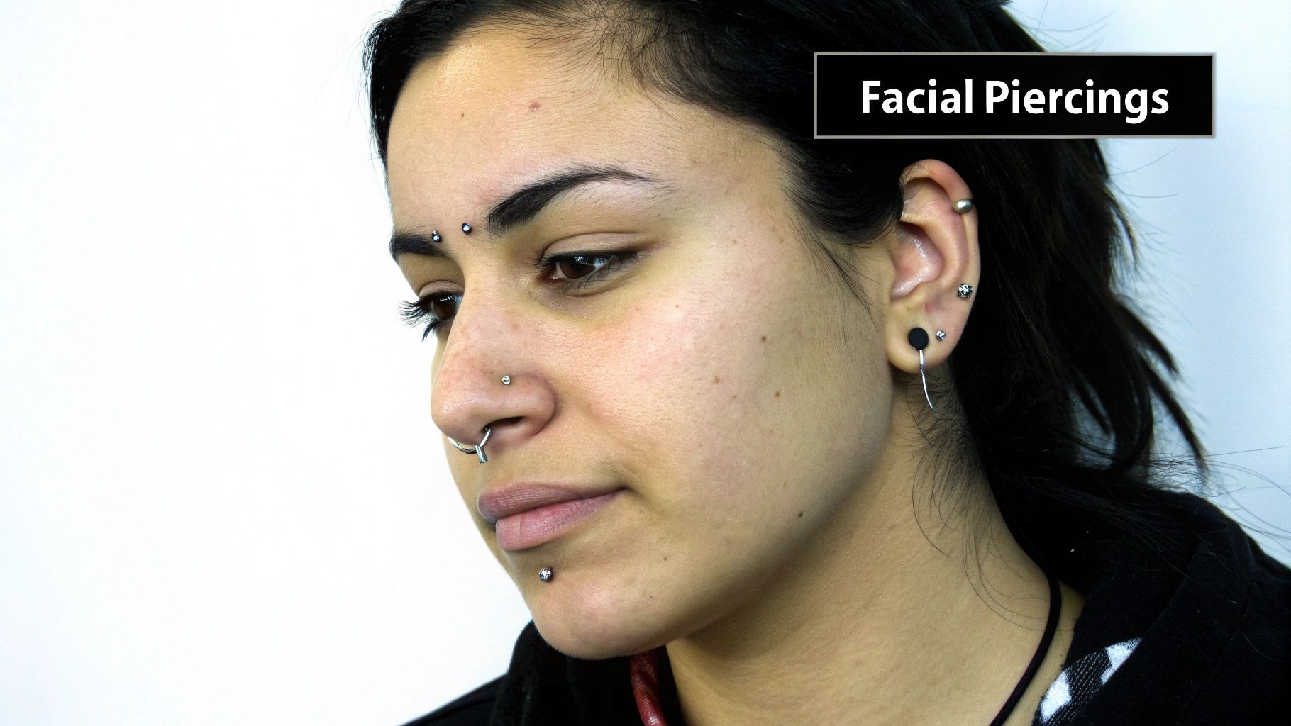 Close-up of a woman with multiple facial and ear piercings, including bridge, septum, nostril, labret, and earlobe.